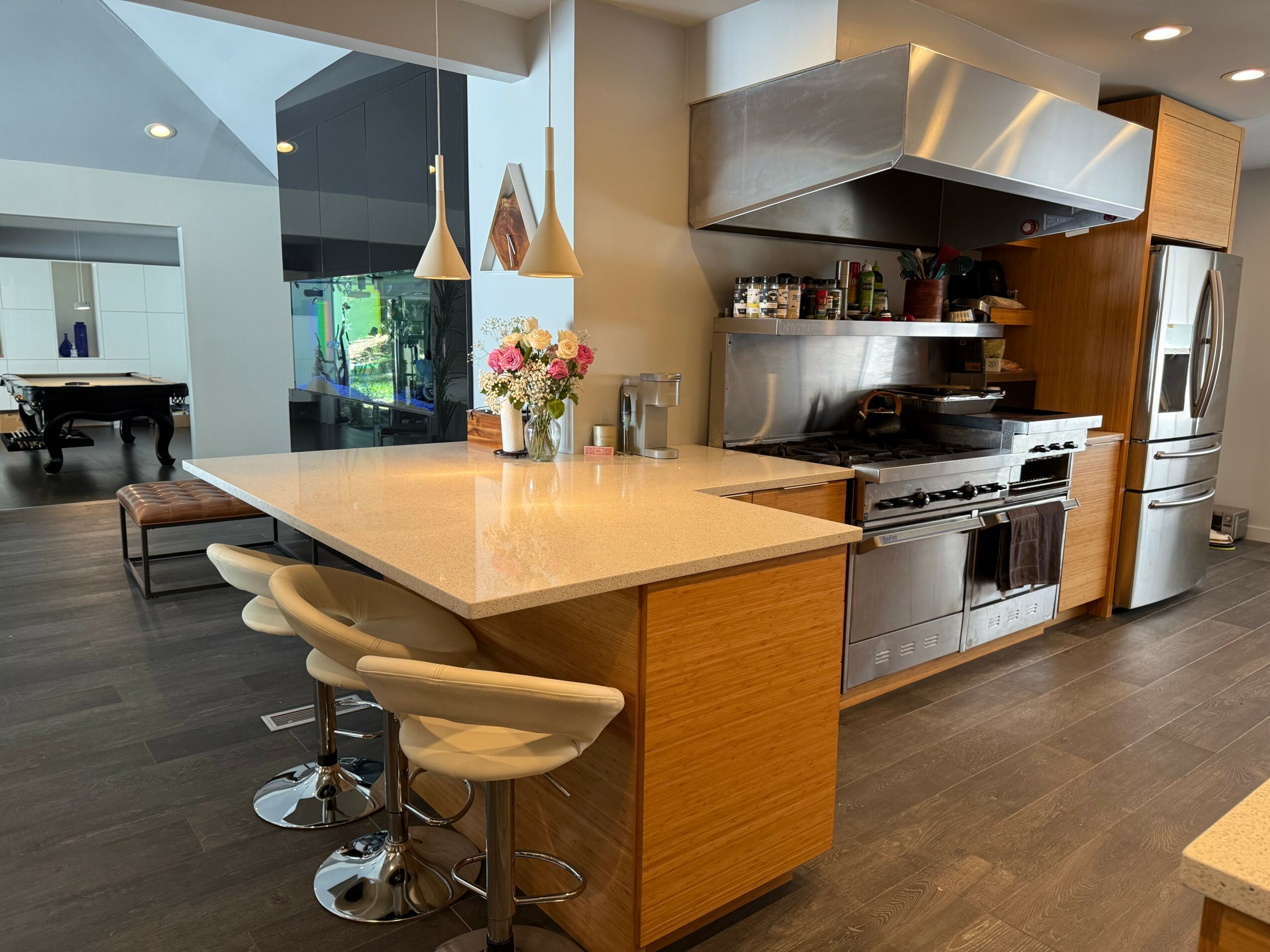 Modern kitchen with a large island, pendant lights, and stainless steel appliances, including a refrigerator and oven, with wooden cabinets.