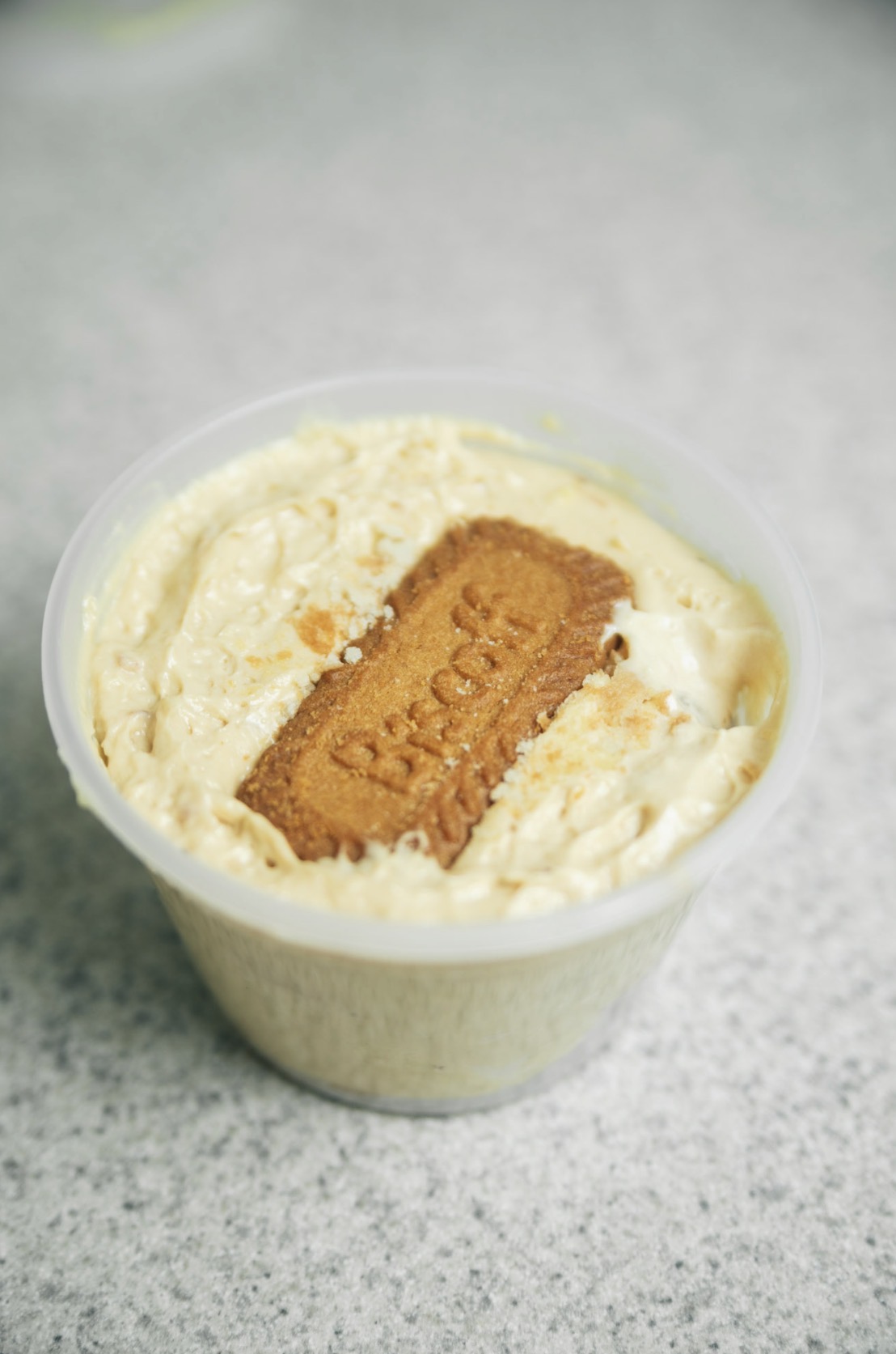 Cup of vanilla ice cream with a rectangular biscuit on top, on a gray surface.