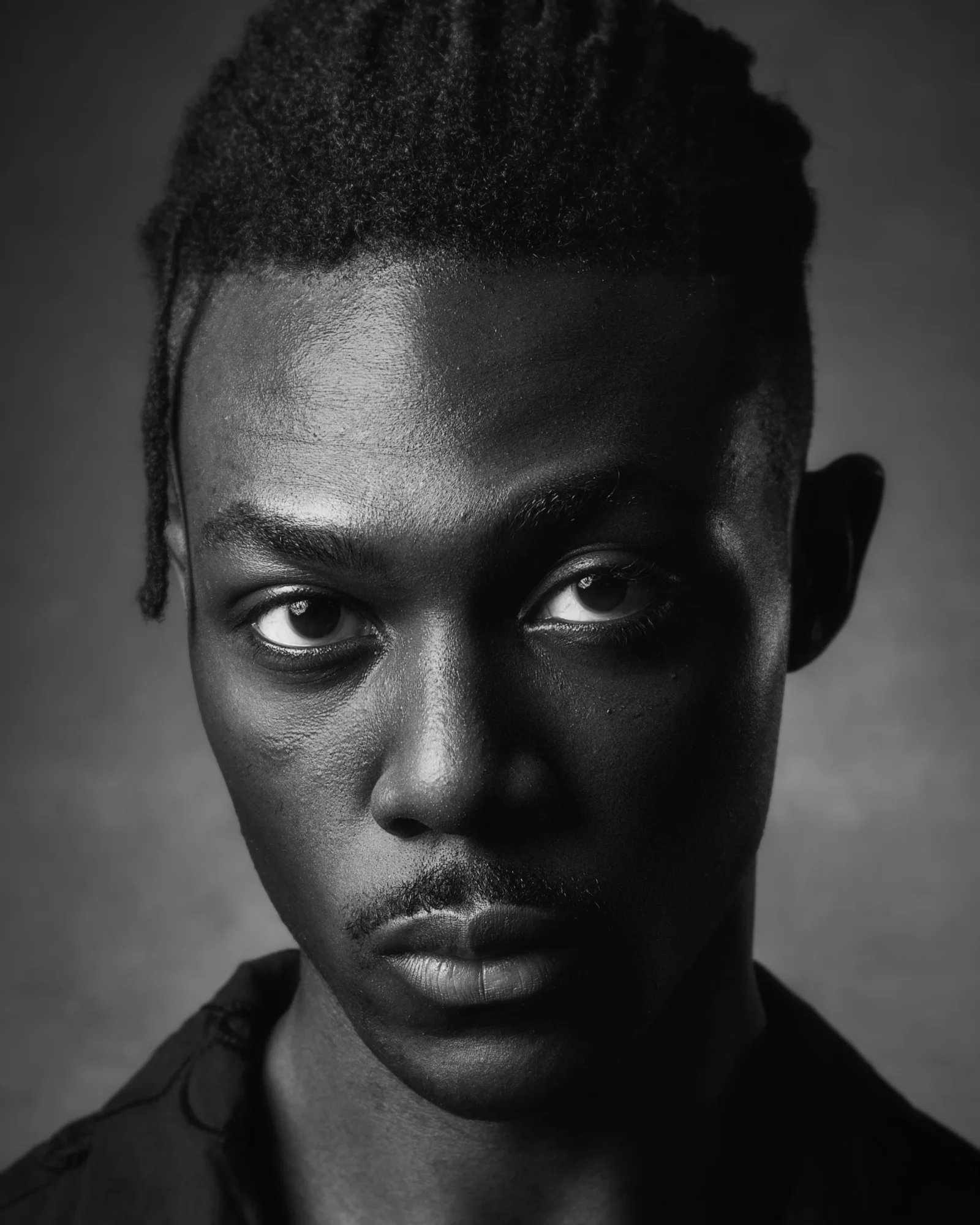 Portrait of a young person with short, textured hair, looking directly at the camera, in black and white.
