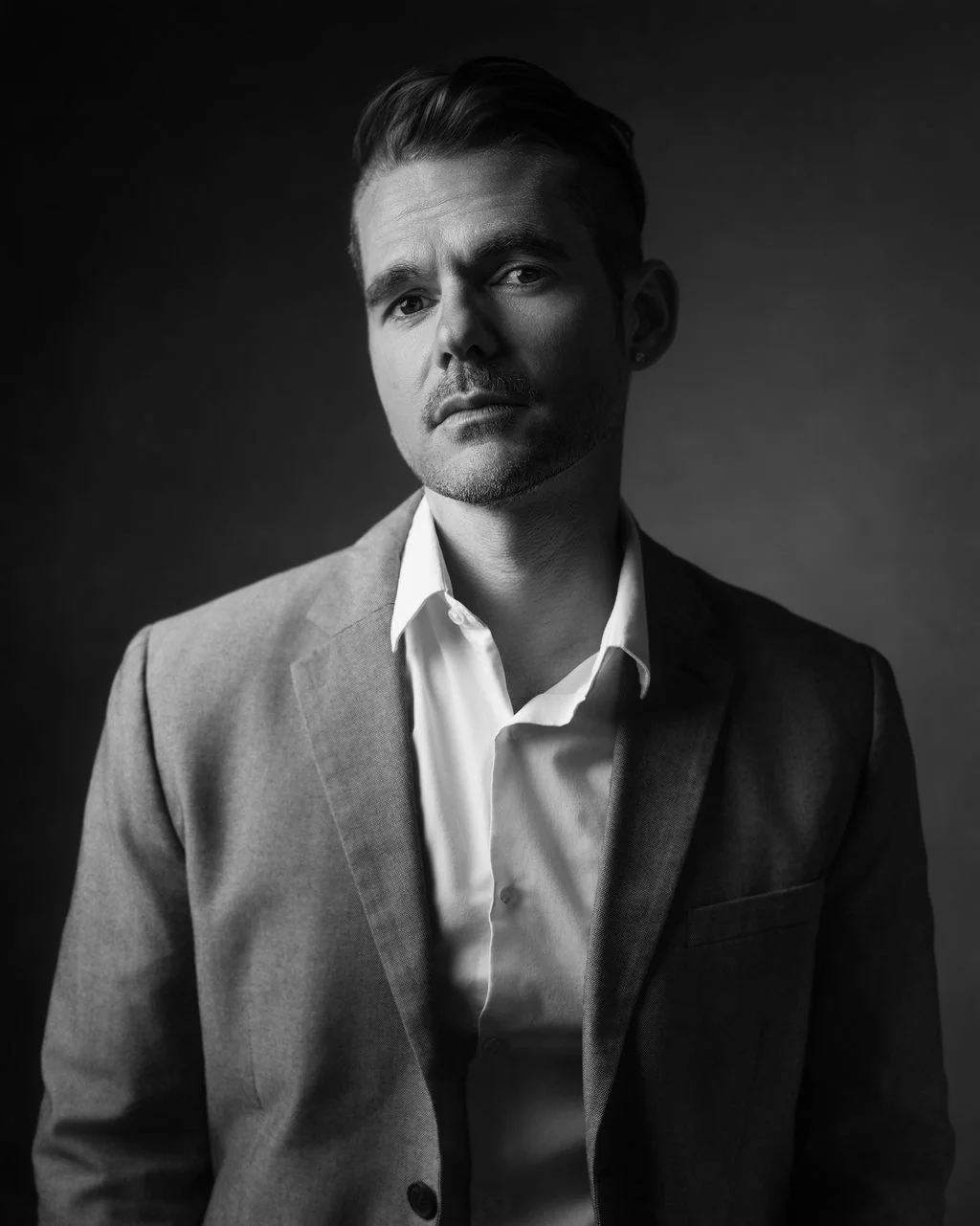 Man in suit with serious expression, looking at camera, black and white portrait.