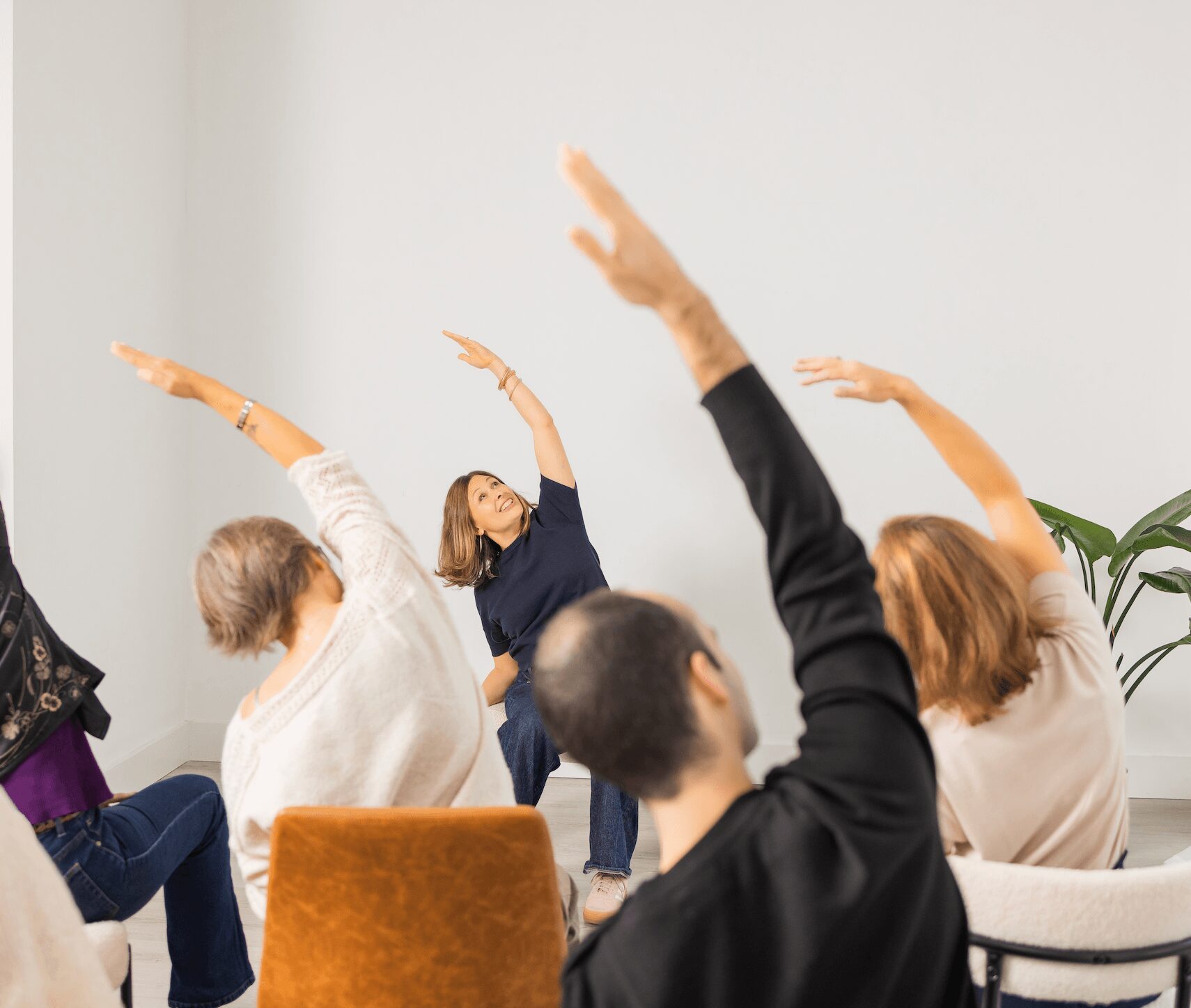 Group of people participating in a seated stretching or yoga session indoors, with a plain white wall background.