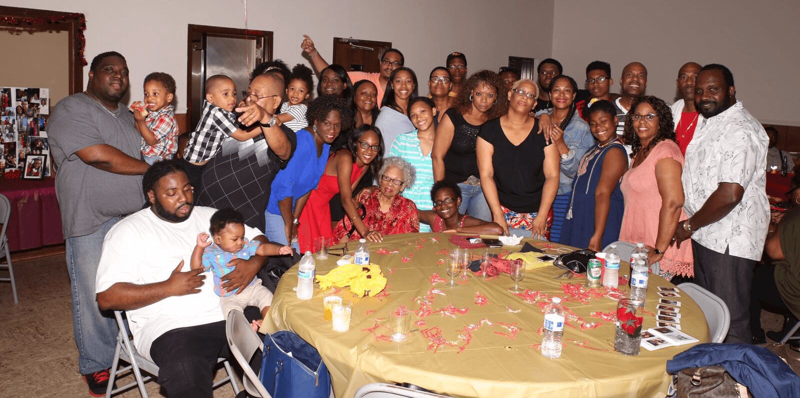 Group of people gathered around a decorated table with cake and drinks, celebrating indoors.