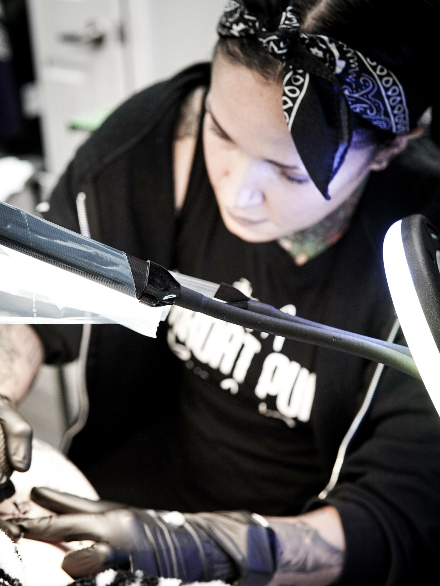 Woman with a bandana working on a tattoo, focused on her task, in a tattoo studio.