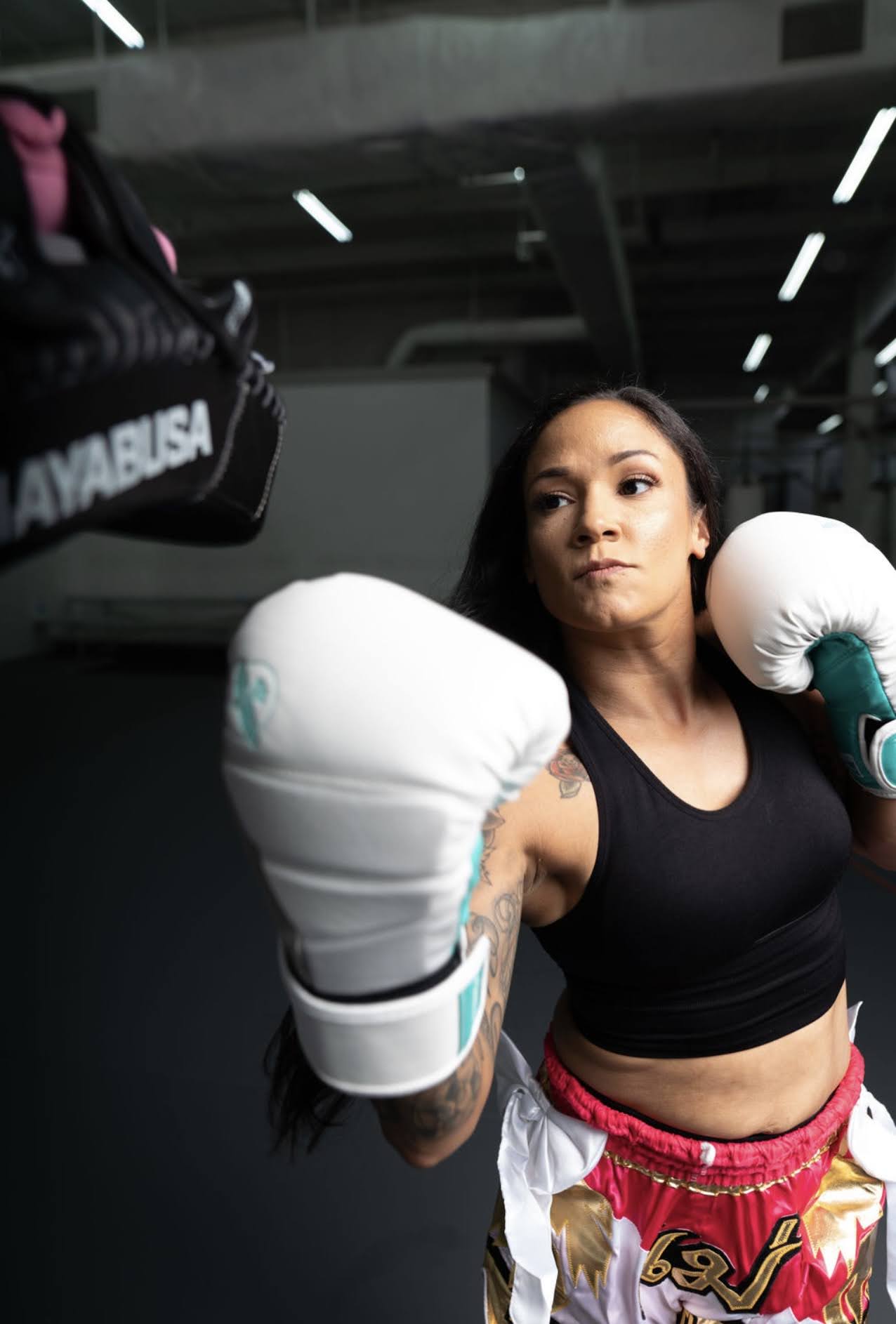 Female boxer in boxing gloves and athletic wear in a gym, preparing for training or a match.