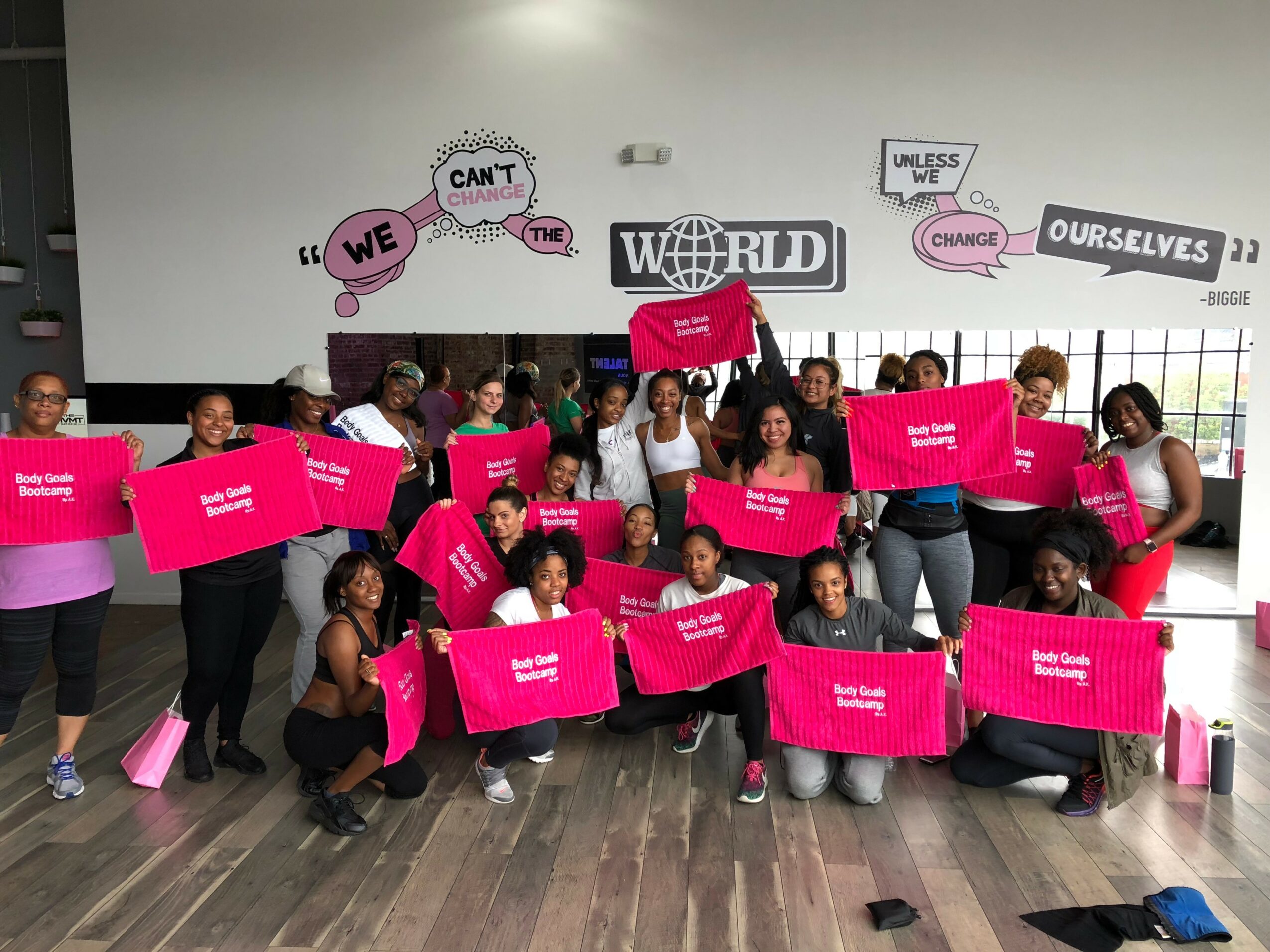 Group of people holding pink signs in a room with motivational wall art, some kneeling and some standing.