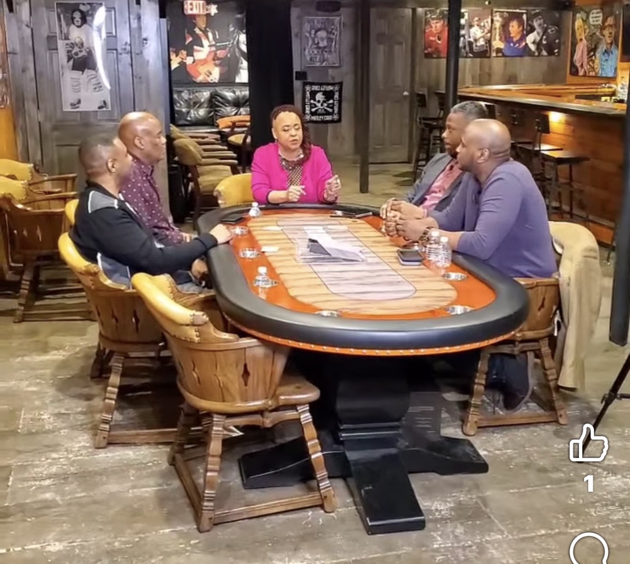 Five people sit around a poker table in a restaurant, engaged in conversation. The woman in pink speaks to four men.