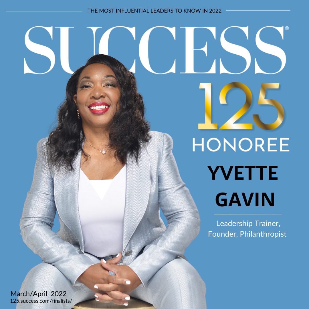 Woman in light gray suit smiling, hands clasped, on blue background with text celebrating 125th honoree, Yvette Gavin.