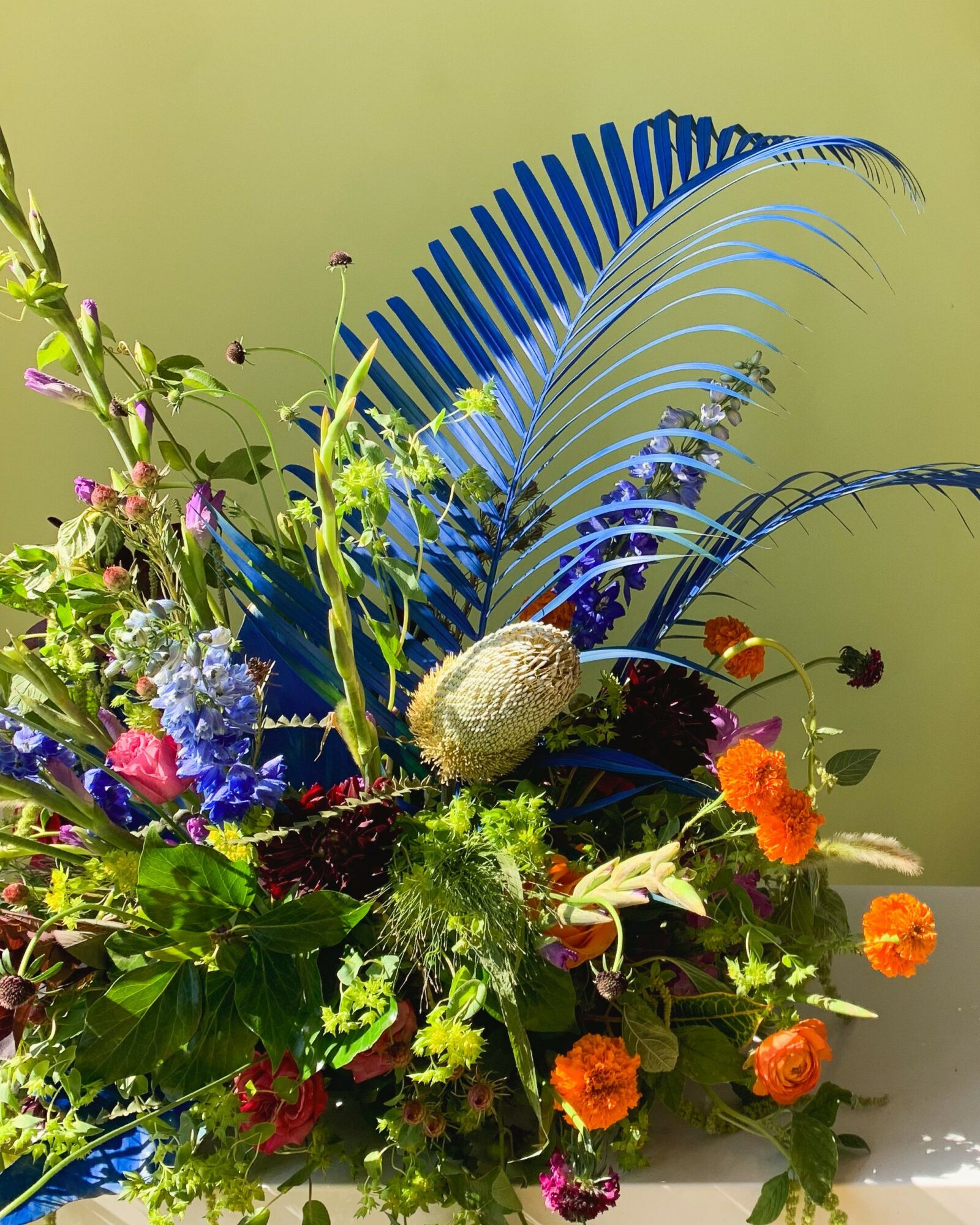 Colorful flower arrangement with green leaves, orange, purple, and blue flowers, and a large blue feather-like decoration.