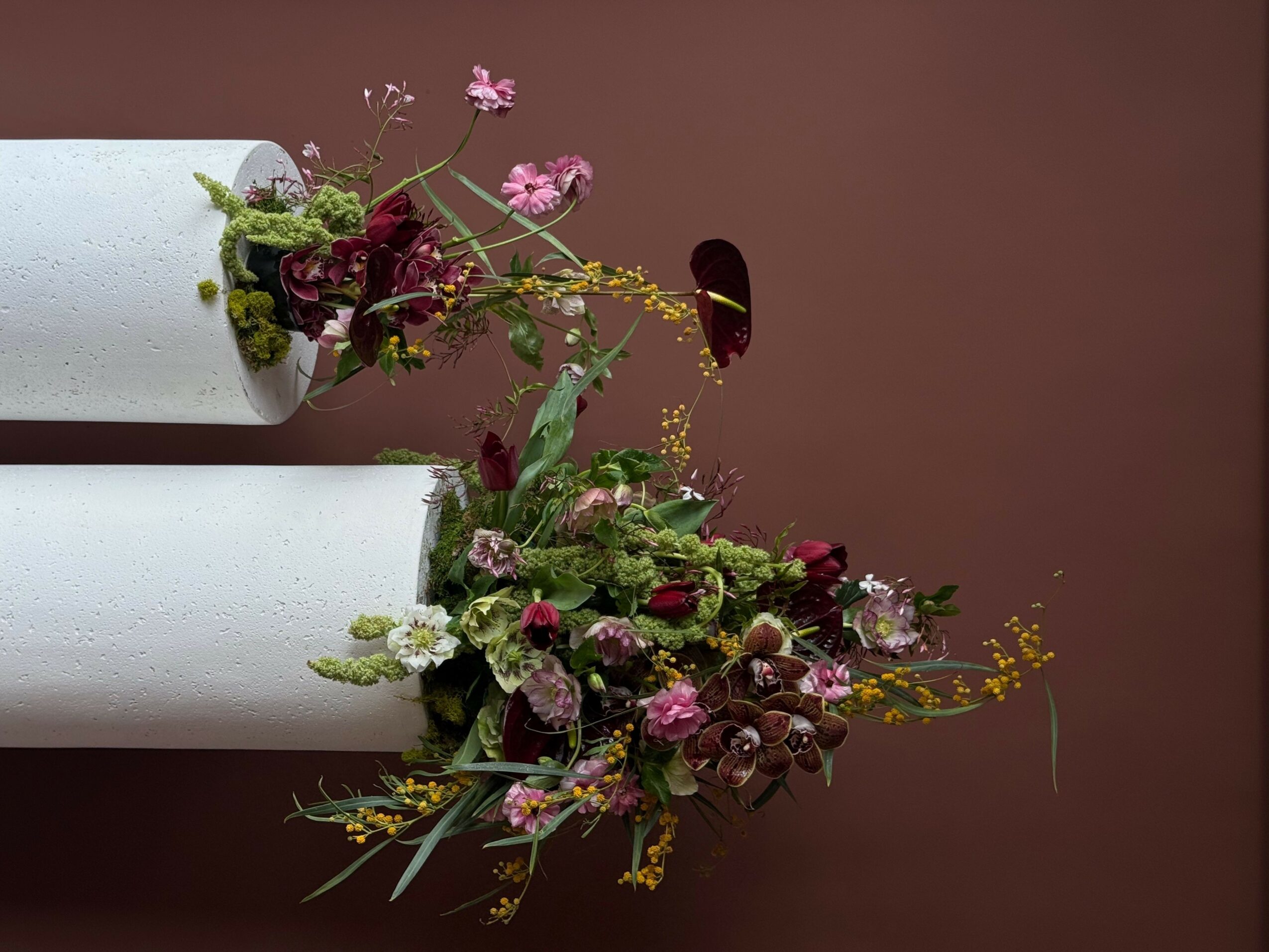 Flower arrangement with pink, purple, and yellow flowers in a white cylindrical vase, viewed sideways.