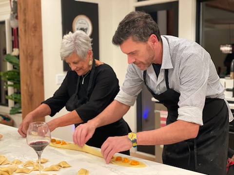 Two people preparing food together in a kitchen, one older woman and one younger man, both focused on their tasks.