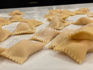 Uncooked ravioli pasta arranged on a floured surface, ready for cooking.