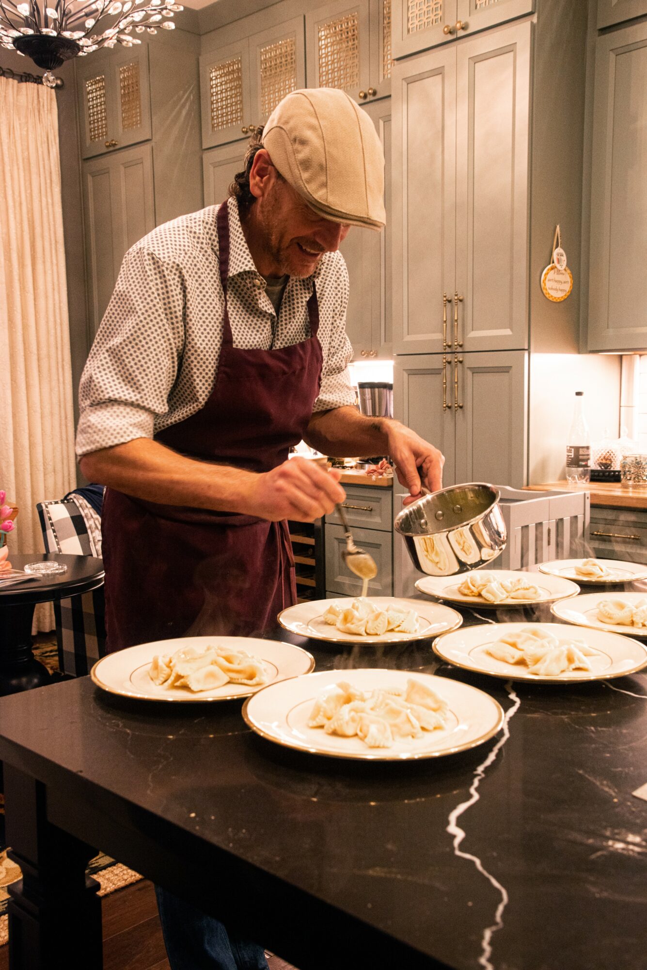 Person wearing a cap and apron preparing food in a kitchen with plates on a black countertop.