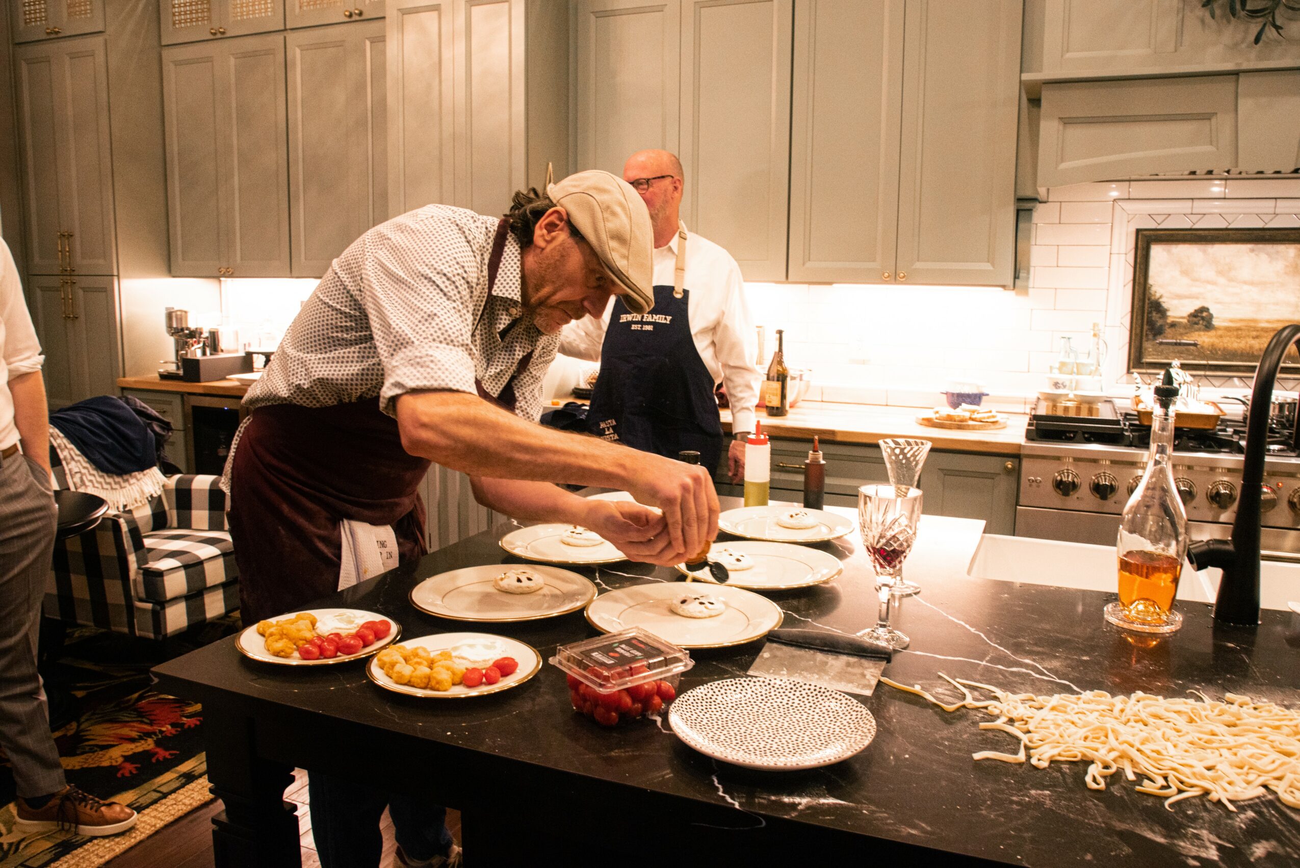 Person preparing food in a kitchen with plates and ingredients on a black countertop, cabinets, and a stove in the background.