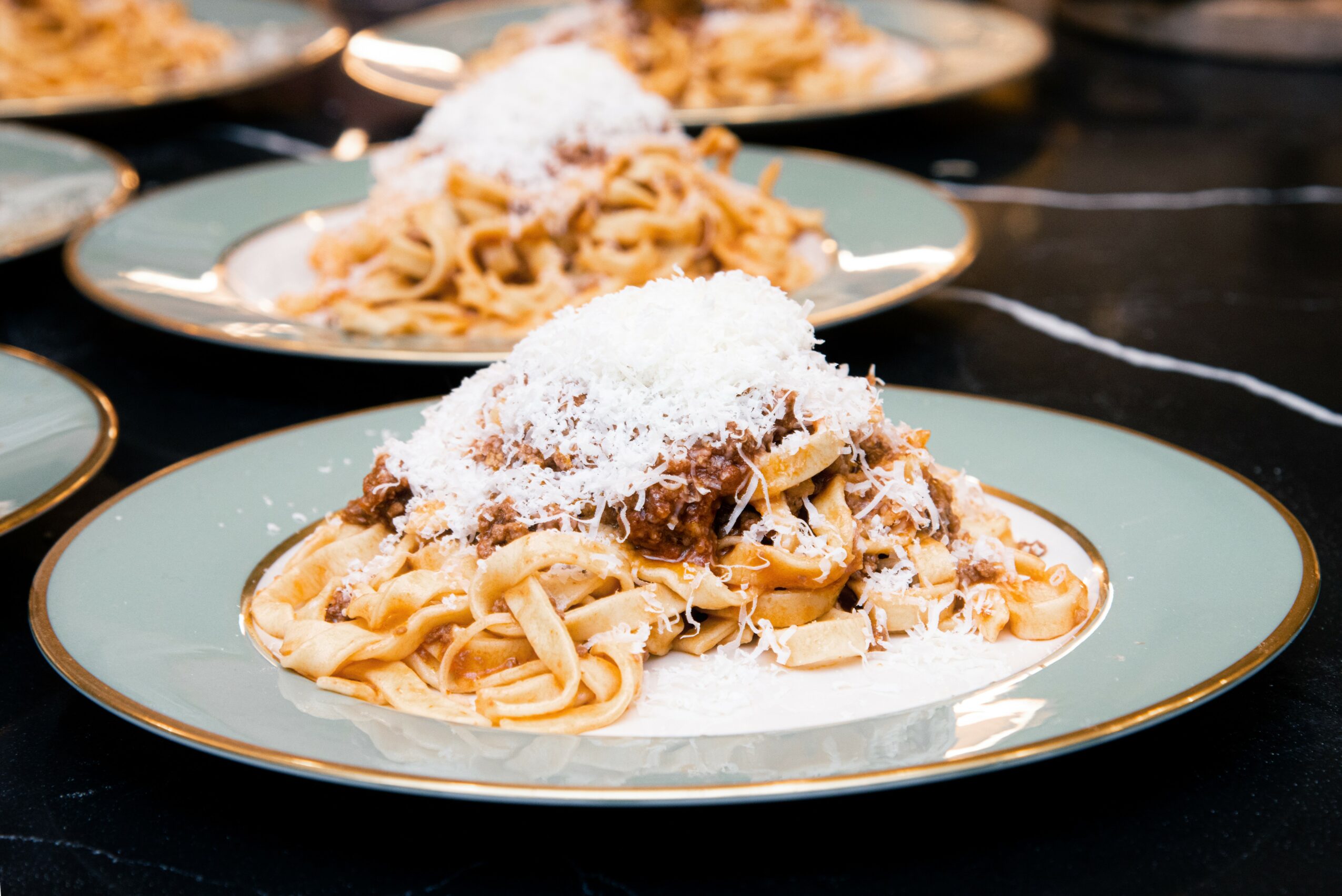 Plate of pasta topped with grated cheese on a decorative plate, with other plates in the background.