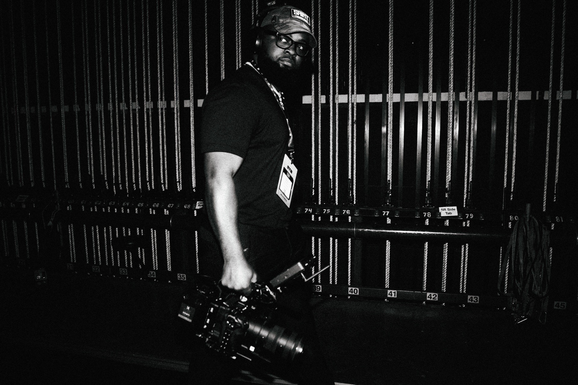 Person holding a camera in a dark environment with vertical bars in the background.