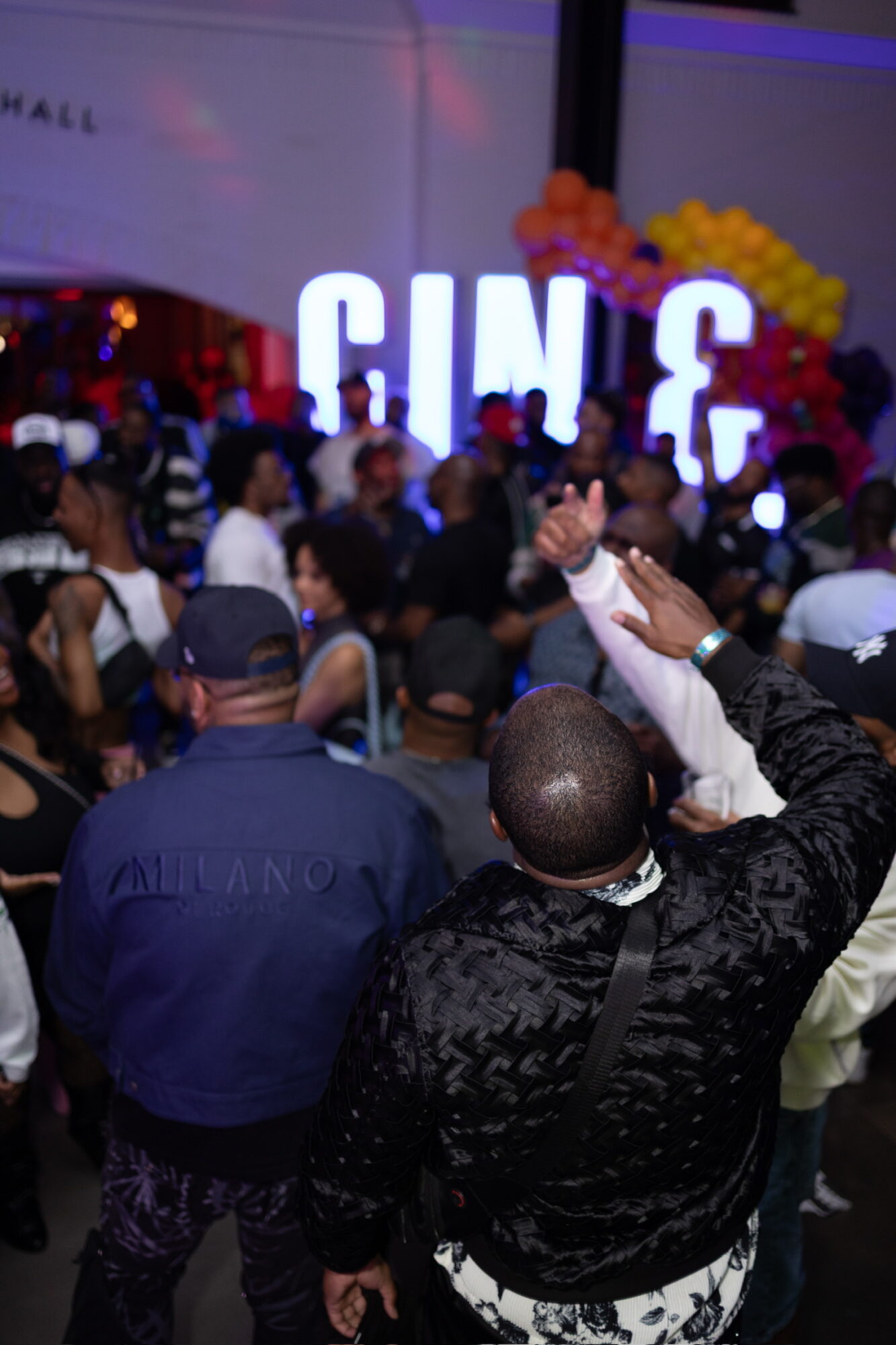 Crowd gathered at an event with large illuminated letters spelling 'GIVE' and colorful balloons in the background.