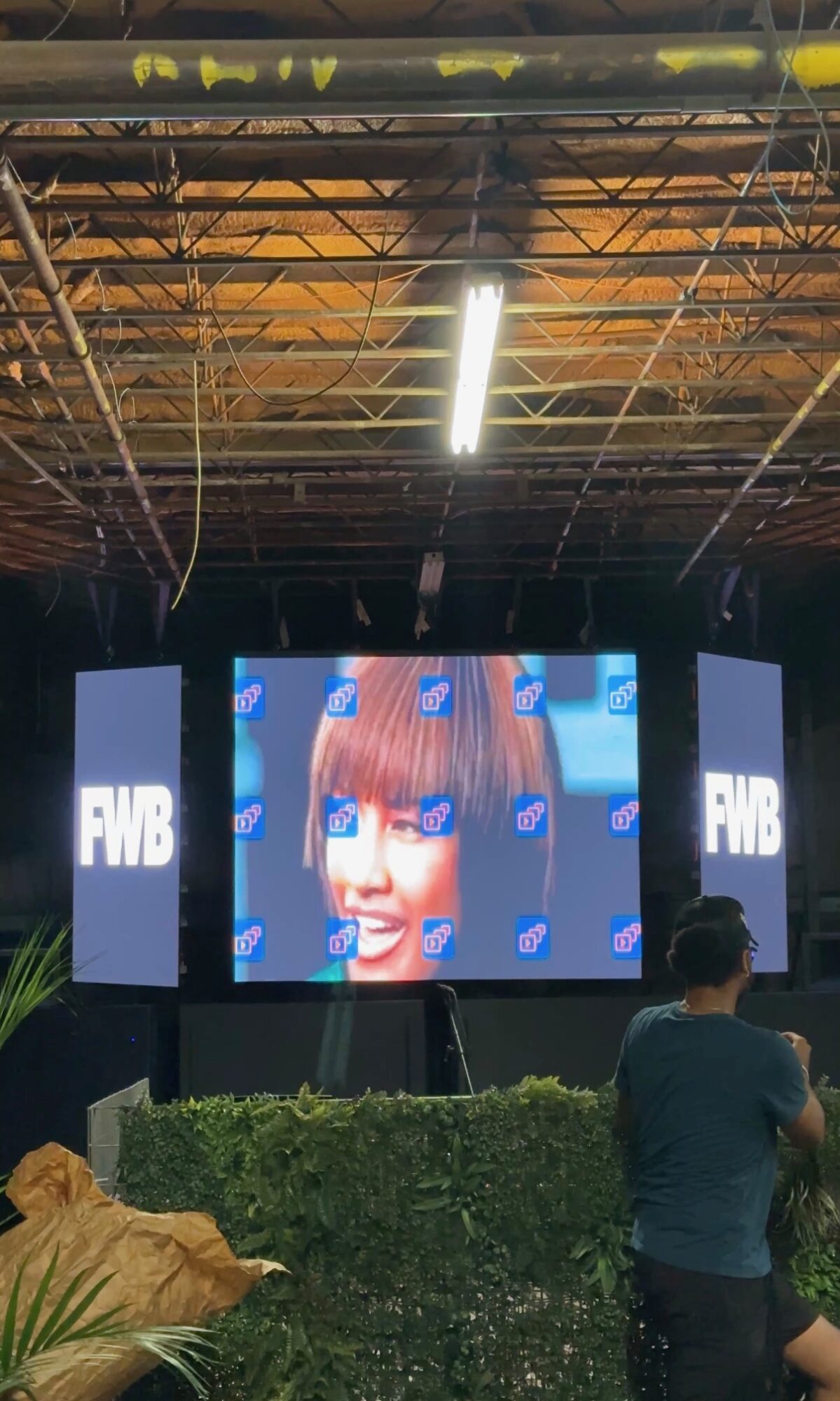 Large screen displays a smiling woman with brown hair, flanked by two vertical screens with the text 'FNB'. People are seated in front of the screens in an indoor setting.