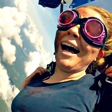 Person wearing goggles, smiling, sky with clouds in background, outdoors, joyful expression