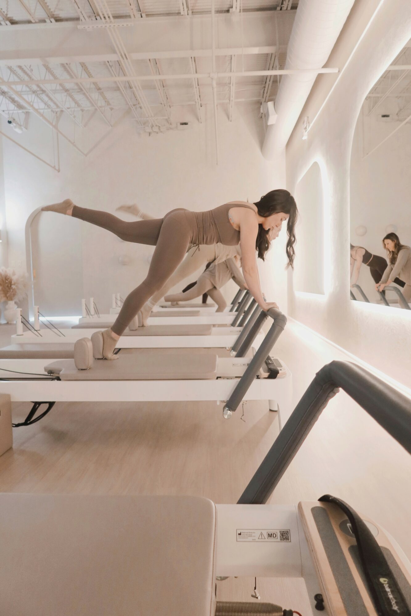 Person in a fitness class using a treadmill, leaning forward with hands on the treadmill's handles, in a bright, modern gym.