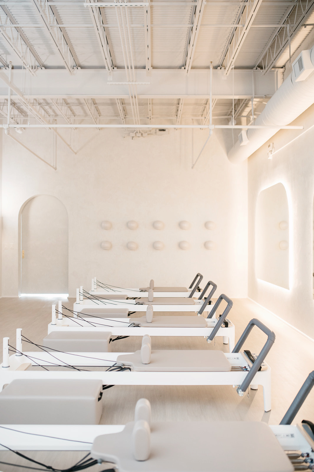 Indoor gym with rowing machines arranged in a row, bright natural light from windows, high ceiling, minimal decor.