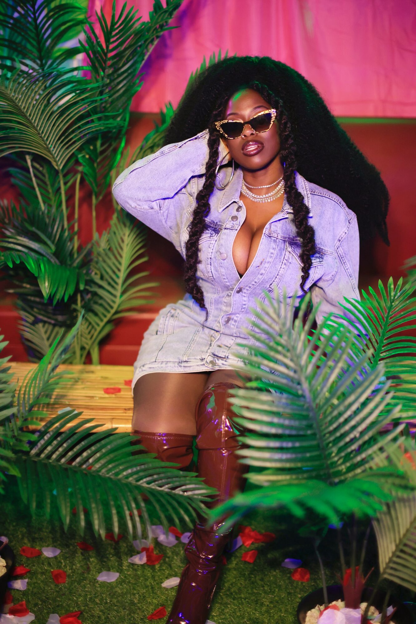 Woman with long curly hair wearing sunglasses, a light purple outfit, and thigh-high boots, surrounded by green plants.
