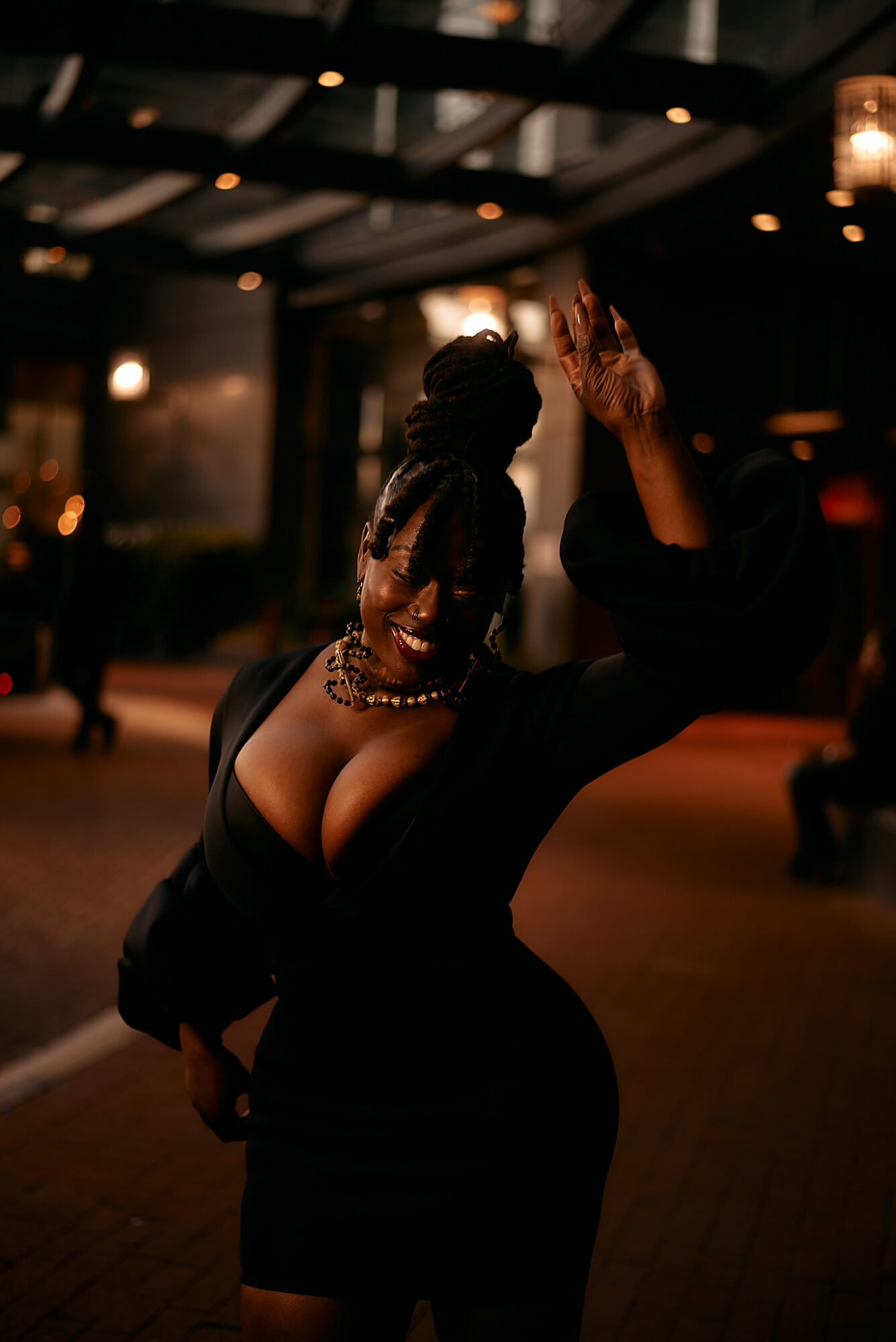 Woman with braided hair and pearl necklace dancing indoors, smiling, with warm lighting and blurred background.