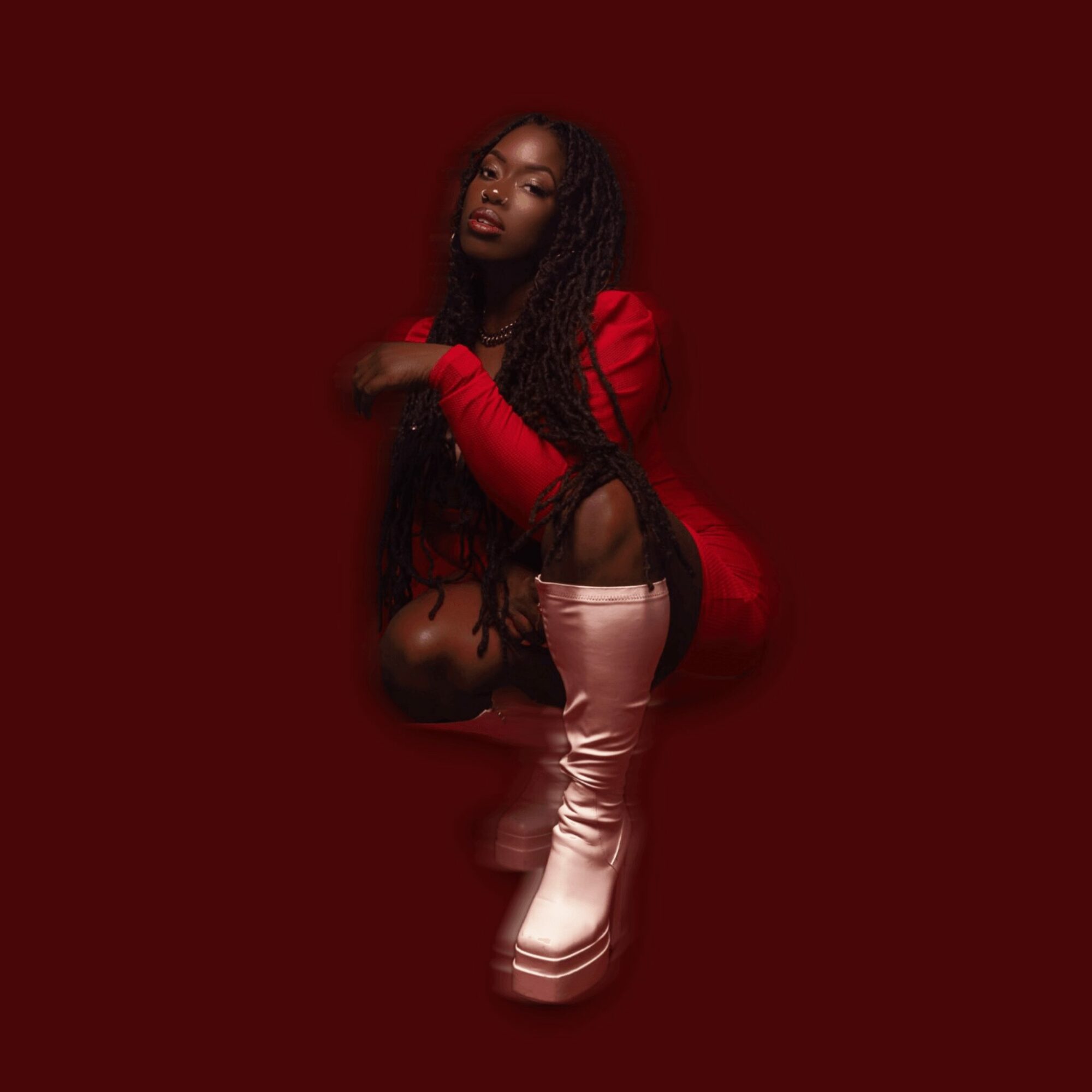 Woman in red top and pink boots crouching against a dark red background.