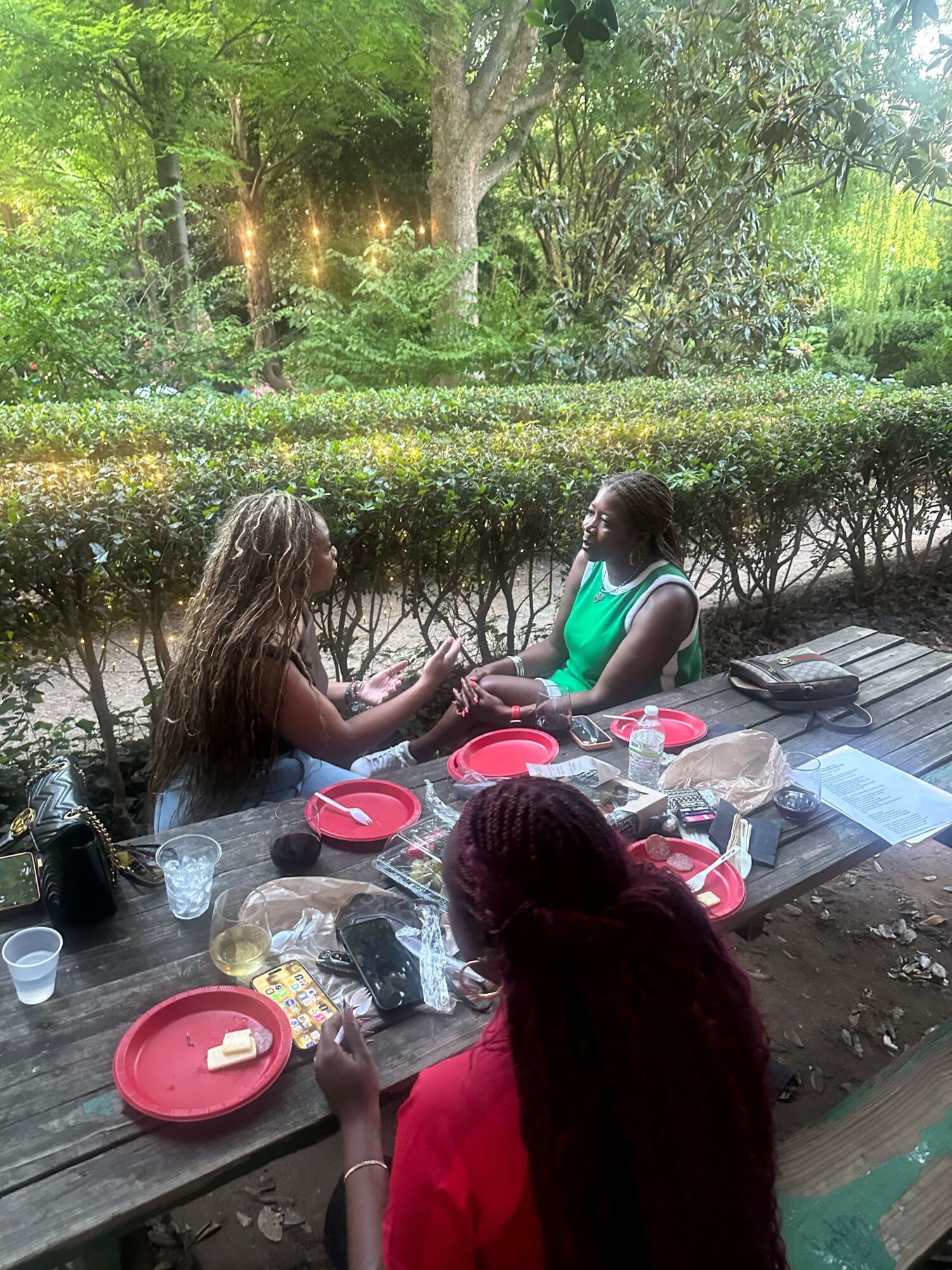 Two children preparing food outdoors at a table with various ingredients and utensils, surrounded by greenery.