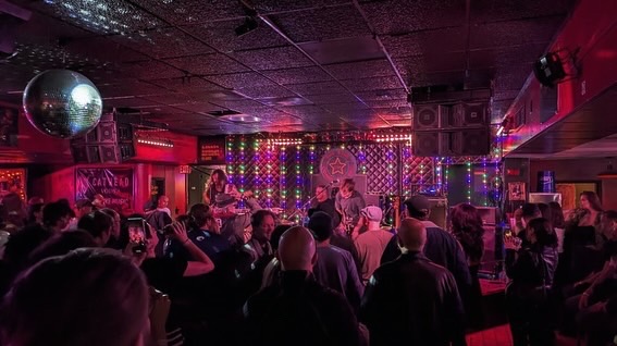 People gathered in a dimly lit nightclub with colorful lights and a disco ball overhead.