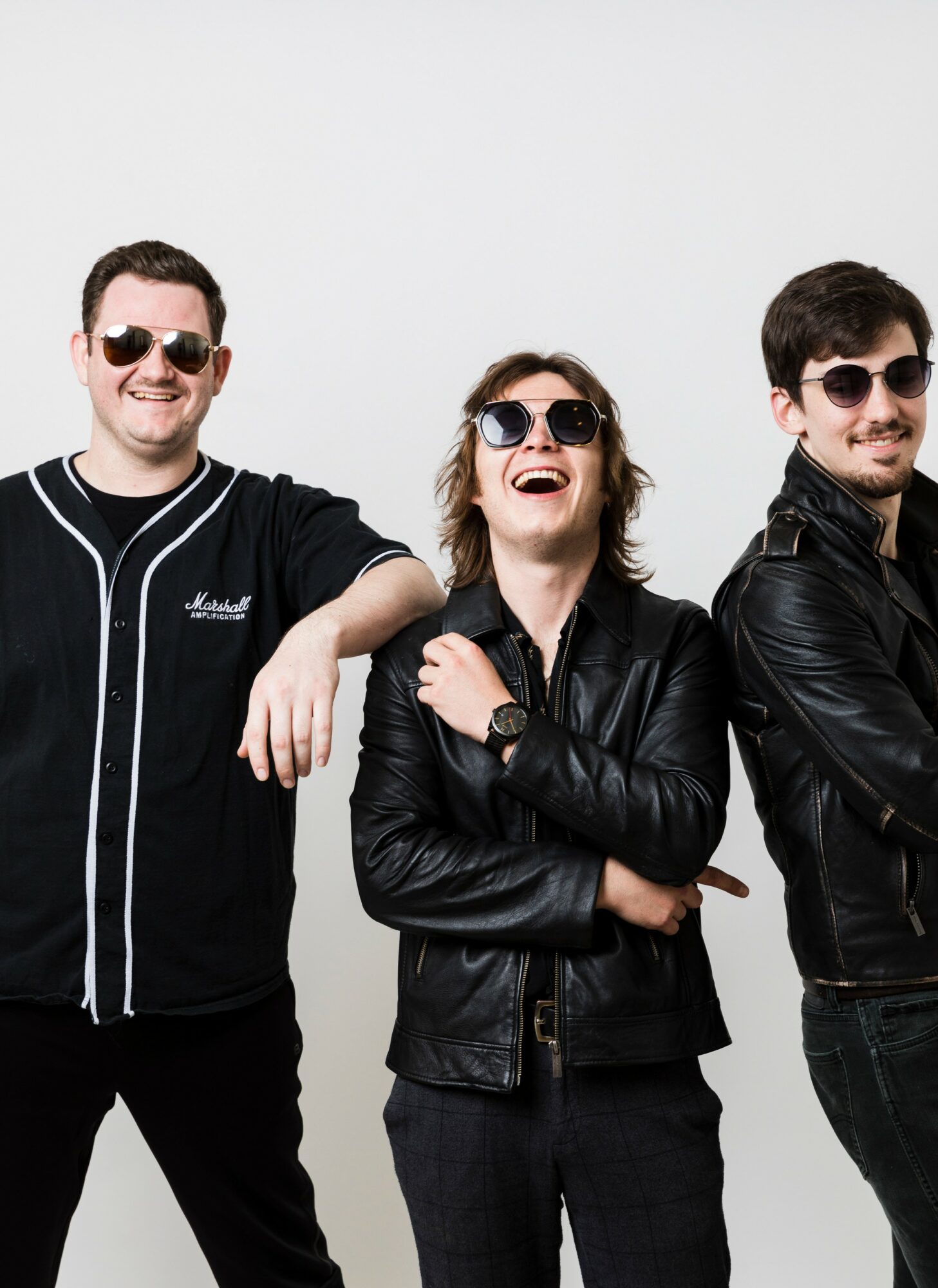 Three people wearing sunglasses and black leather jackets, smiling and standing against a plain white background.
