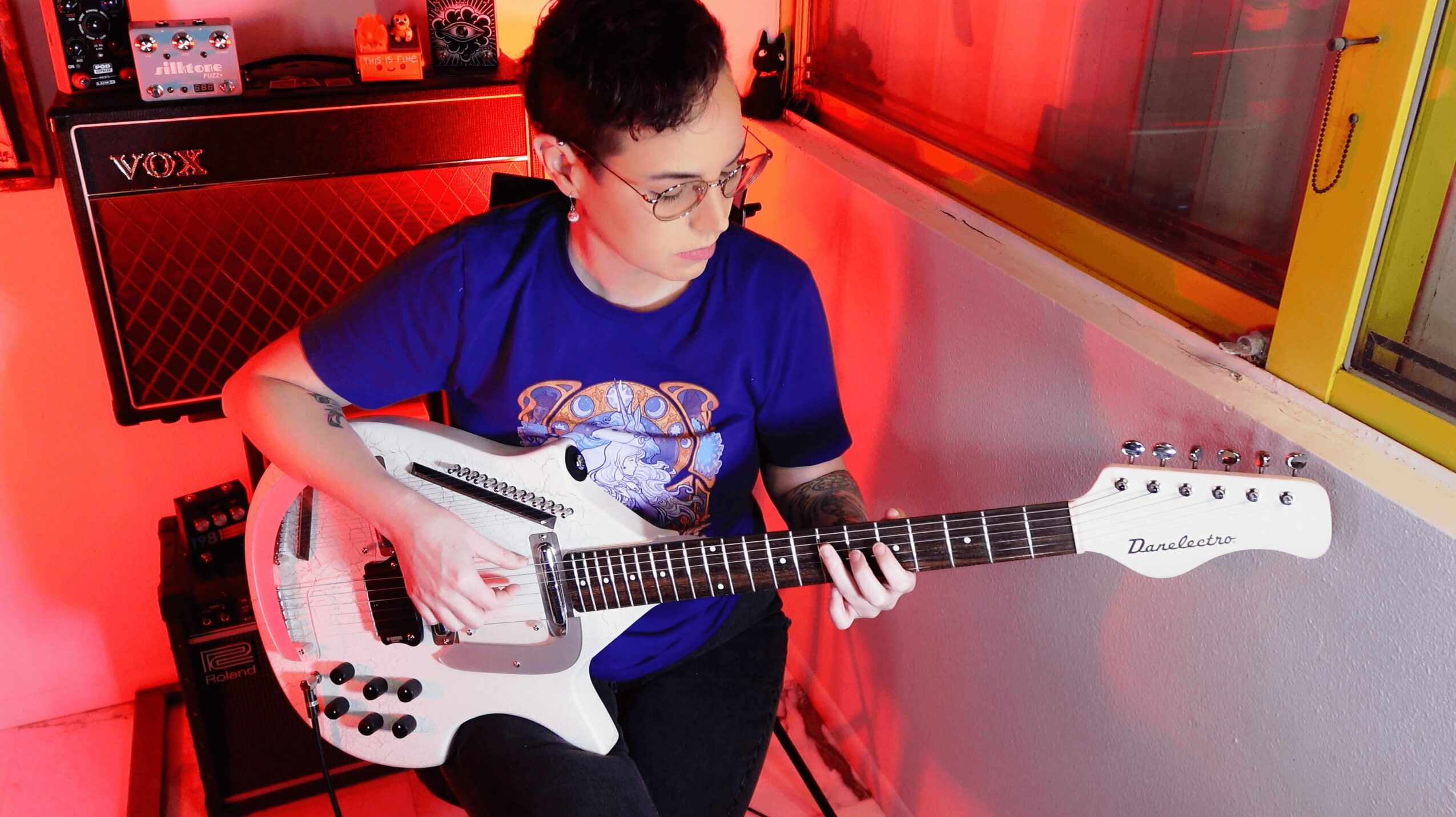 Child with glasses playing a white electric guitar in a room with red lighting.