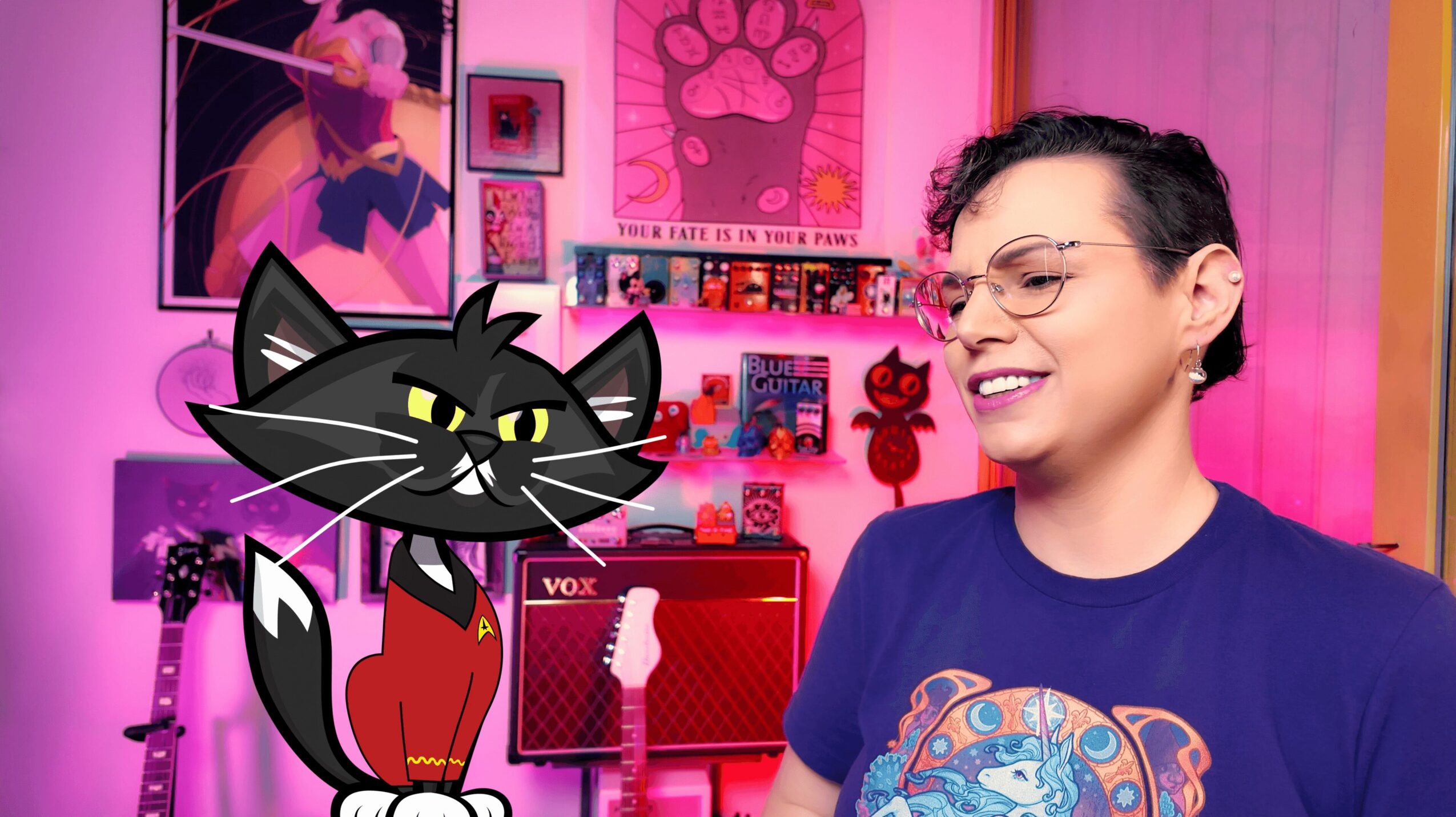 Person with short dark hair and glasses smiling in a colorful room with pink and purple decor, a cartoon cat character nearby.