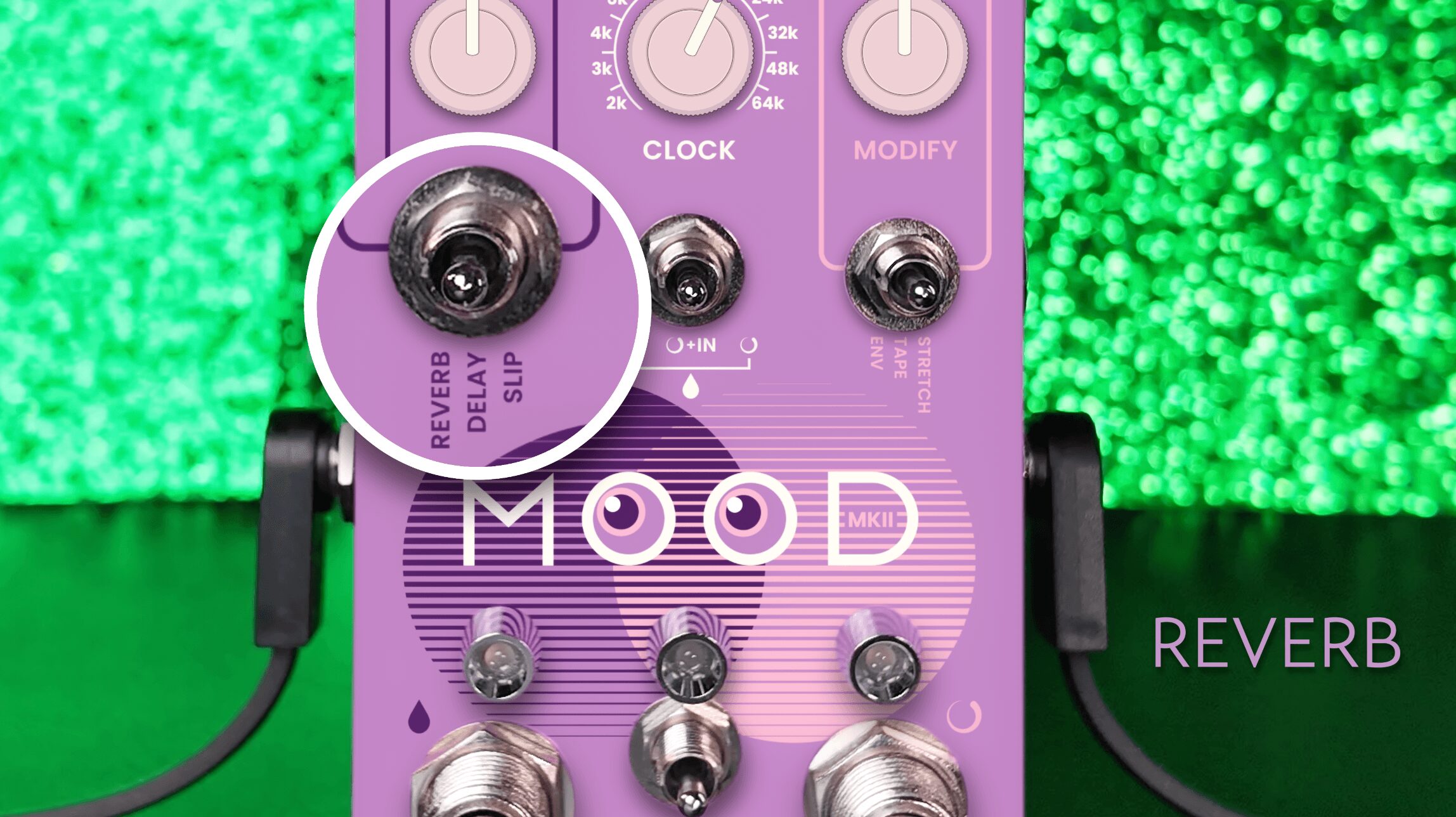 Purple guitar effects pedal labeled 'MOOD' with knobs and switches, connected to cables, against a green textured background.