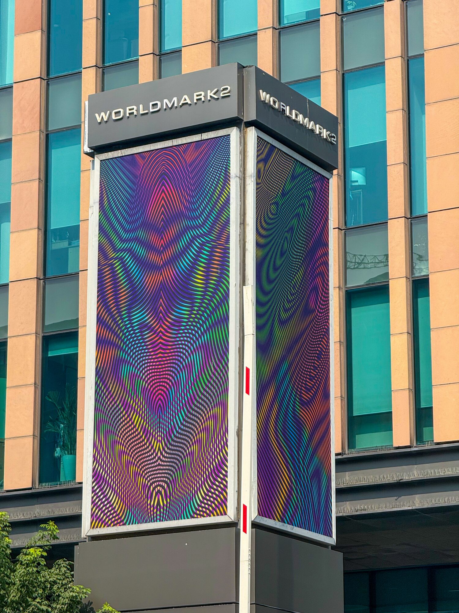 Tall digital billboard with colorful patterns, mounted on a building with blue and orange vertical panels, labeled 'Worldmark2'.