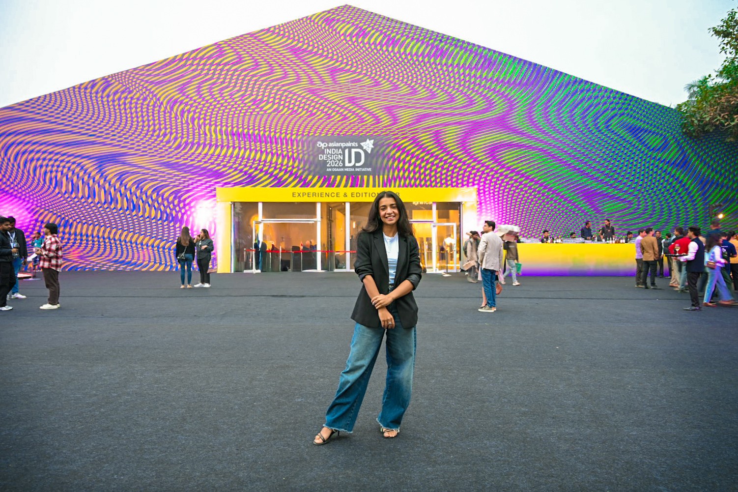 Woman standing in front of a large, colorful building with a patterned facade and a crowd nearby.