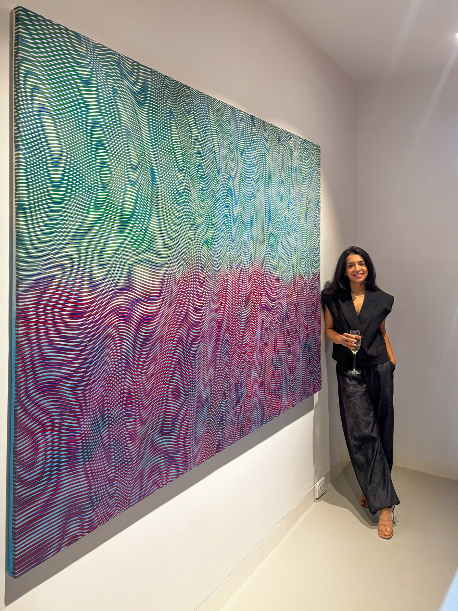Woman standing next to a large colorful abstract painting on a white gallery wall.