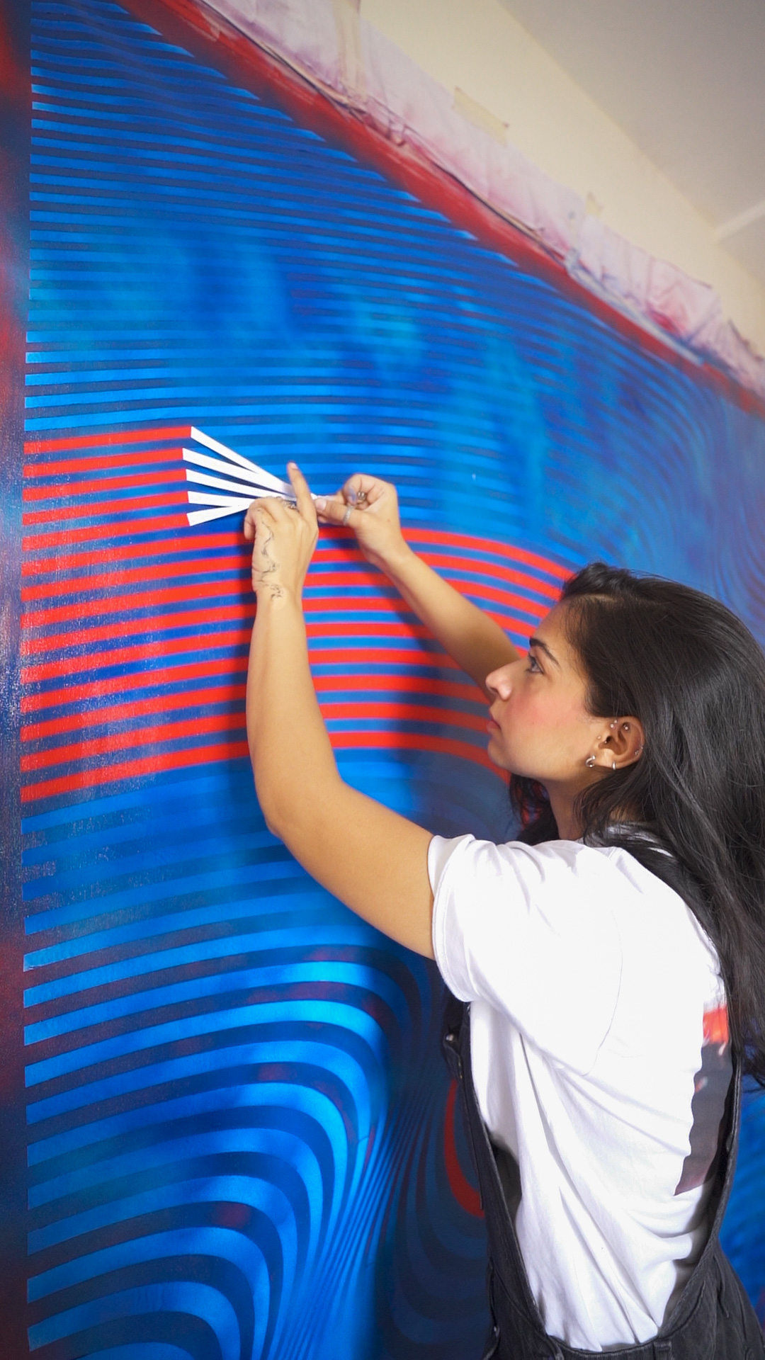 Girl in white shirt attaching striped paper to a blue and red patterned wall.