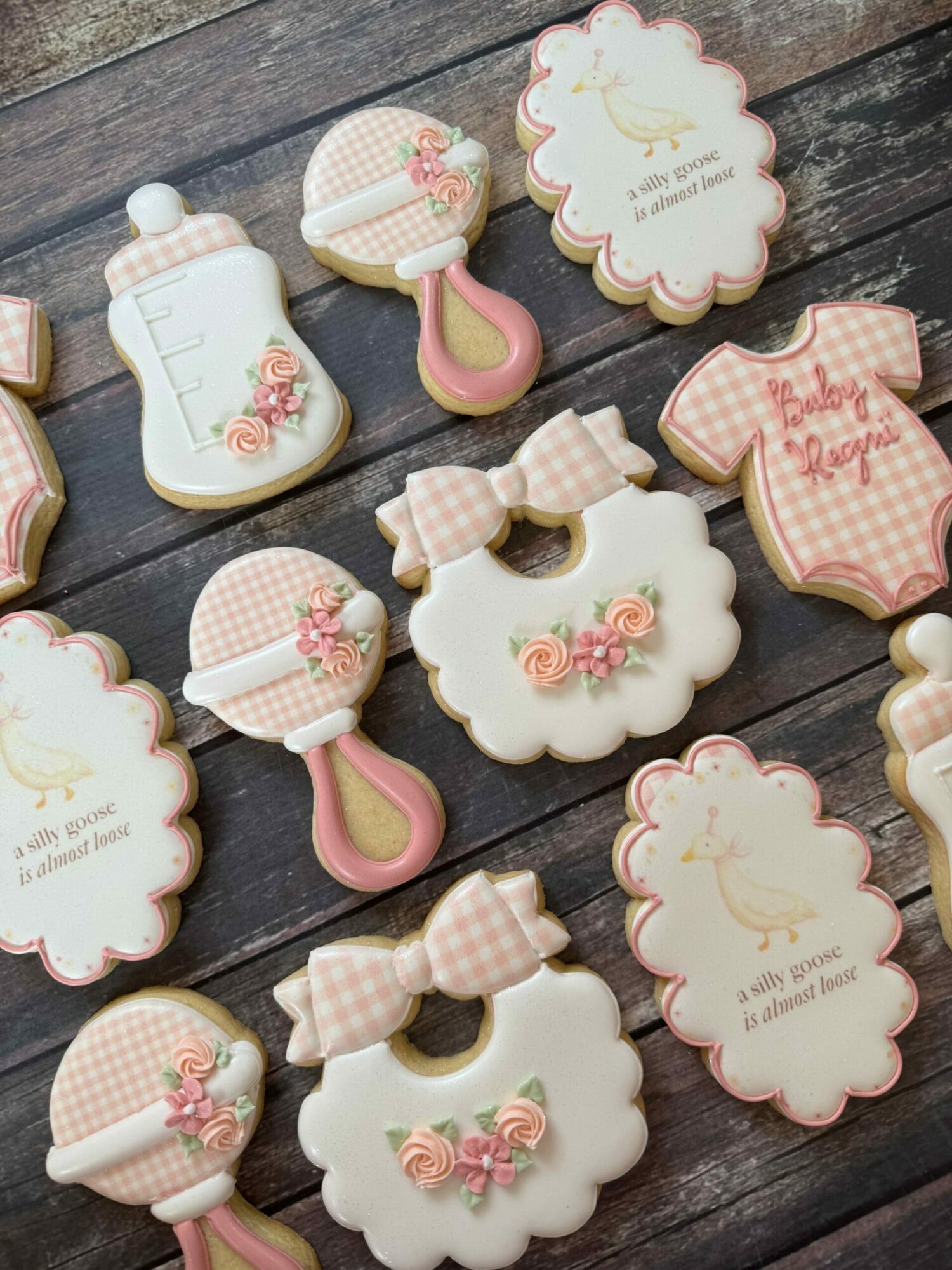 Decorative cookies with pink and white patterns, floral designs, and text, arranged on a dark wooden surface.