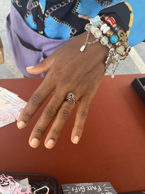 Hand with multiple bracelets and a ring, resting on a red surface, with a black object nearby.