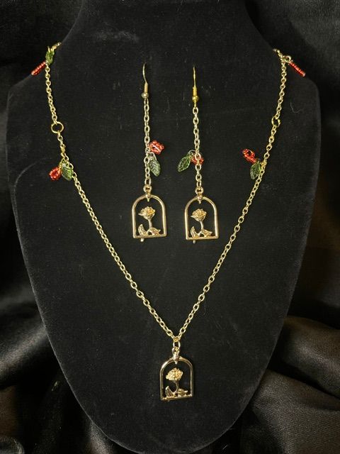 Gold jewelry set with necklace, earrings, and pendant displayed on black velvet background, featuring small red and green decorative elements.
