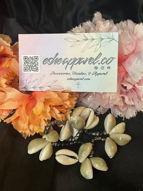 Business card with floral design, surrounded by pink and orange flowers and white seashells on black fabric.