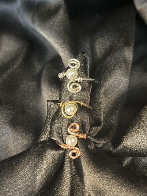 Three pairs of earrings with pearls and metal hooks on black fabric, arranged in a row.