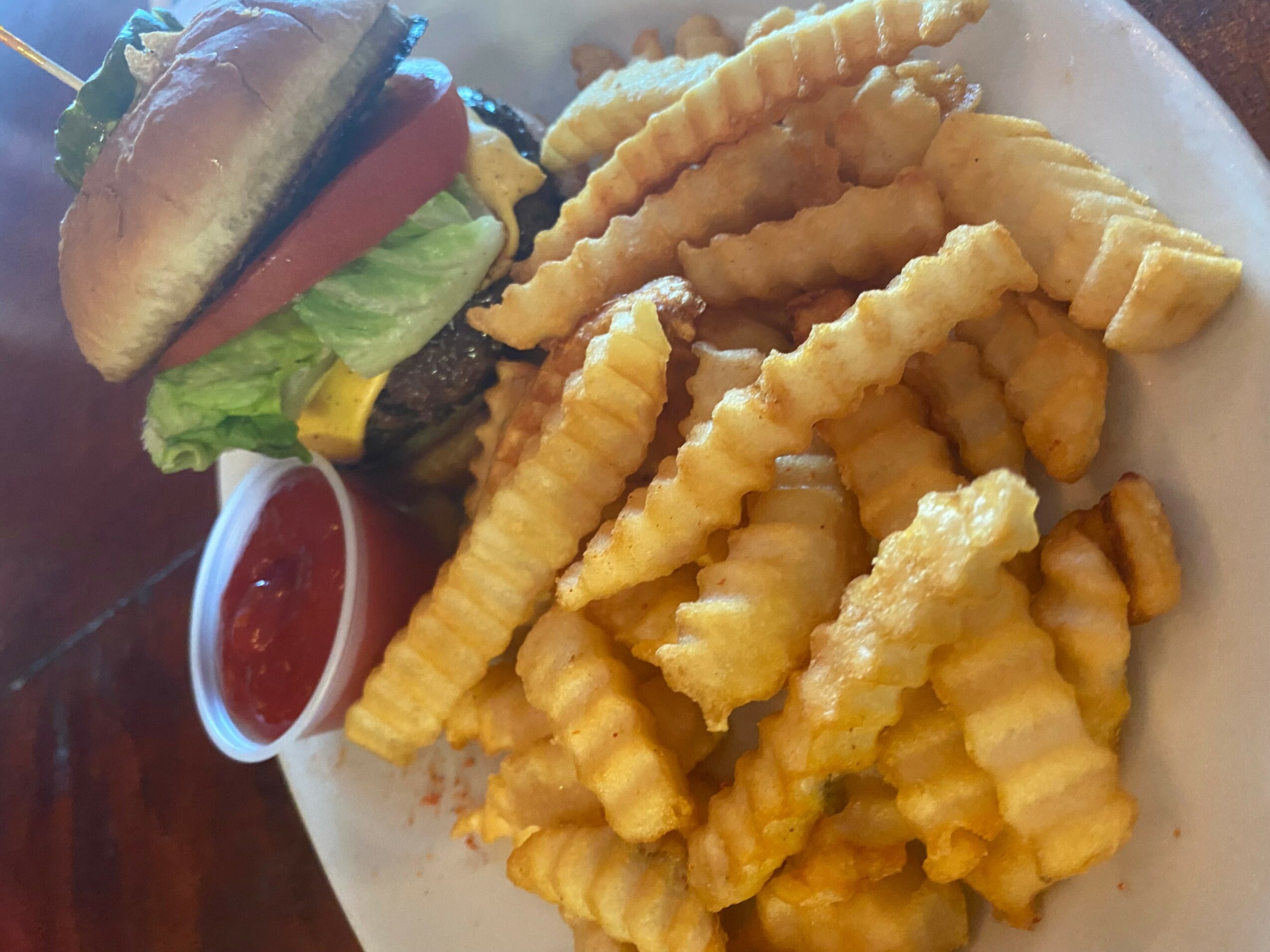 Plate with crinkle-cut French fries, a small cup of ketchup, and a burger with lettuce, tomato, cheese, and a bun