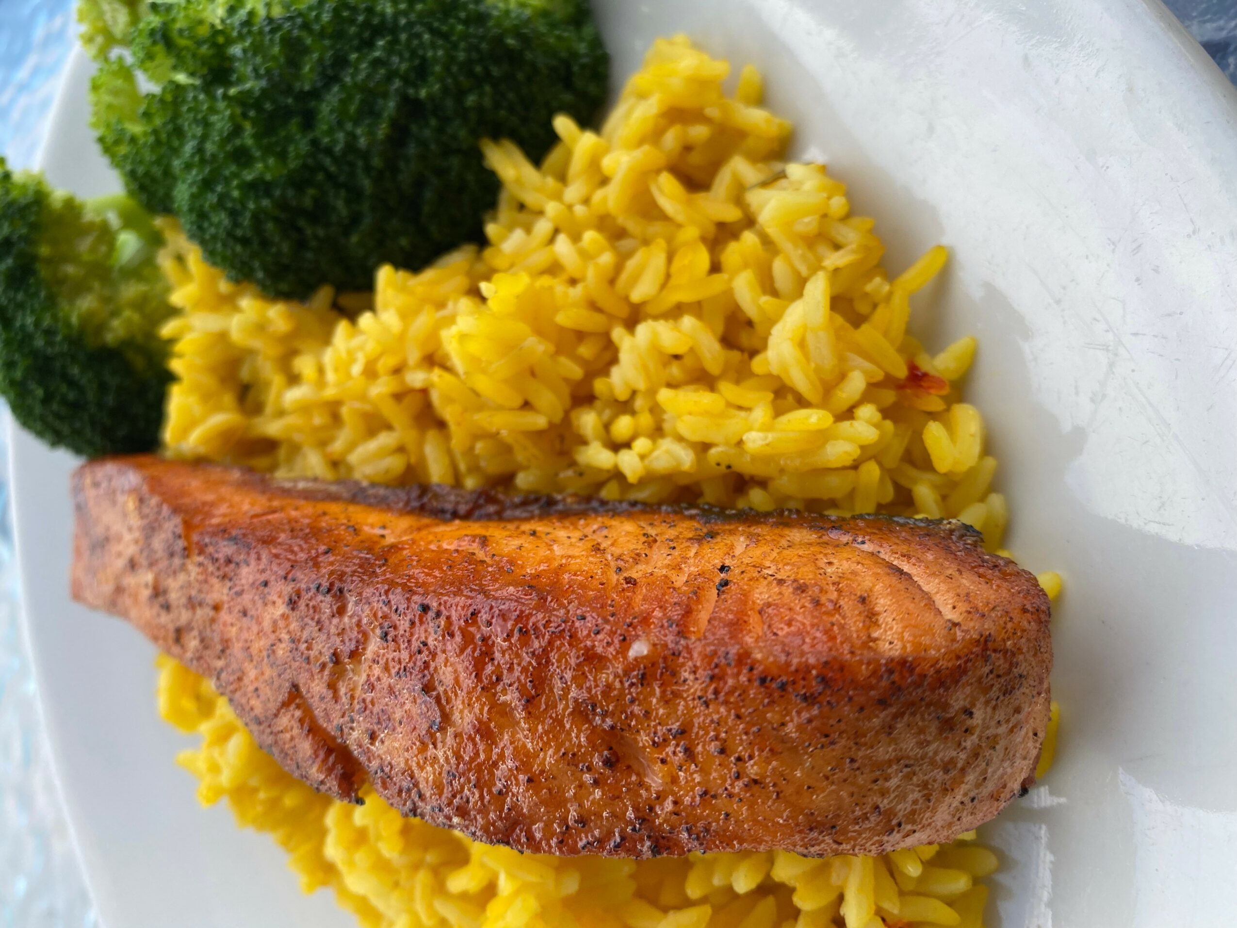 Fried fish fillet with yellow rice and broccoli on a white plate.