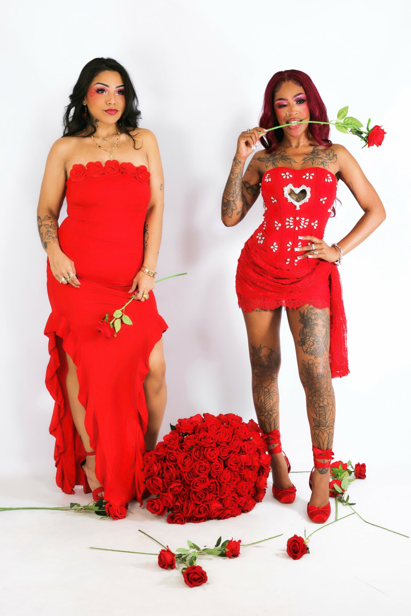 Two women in red dresses holding roses, one with a bouquet on the floor, against a white background.