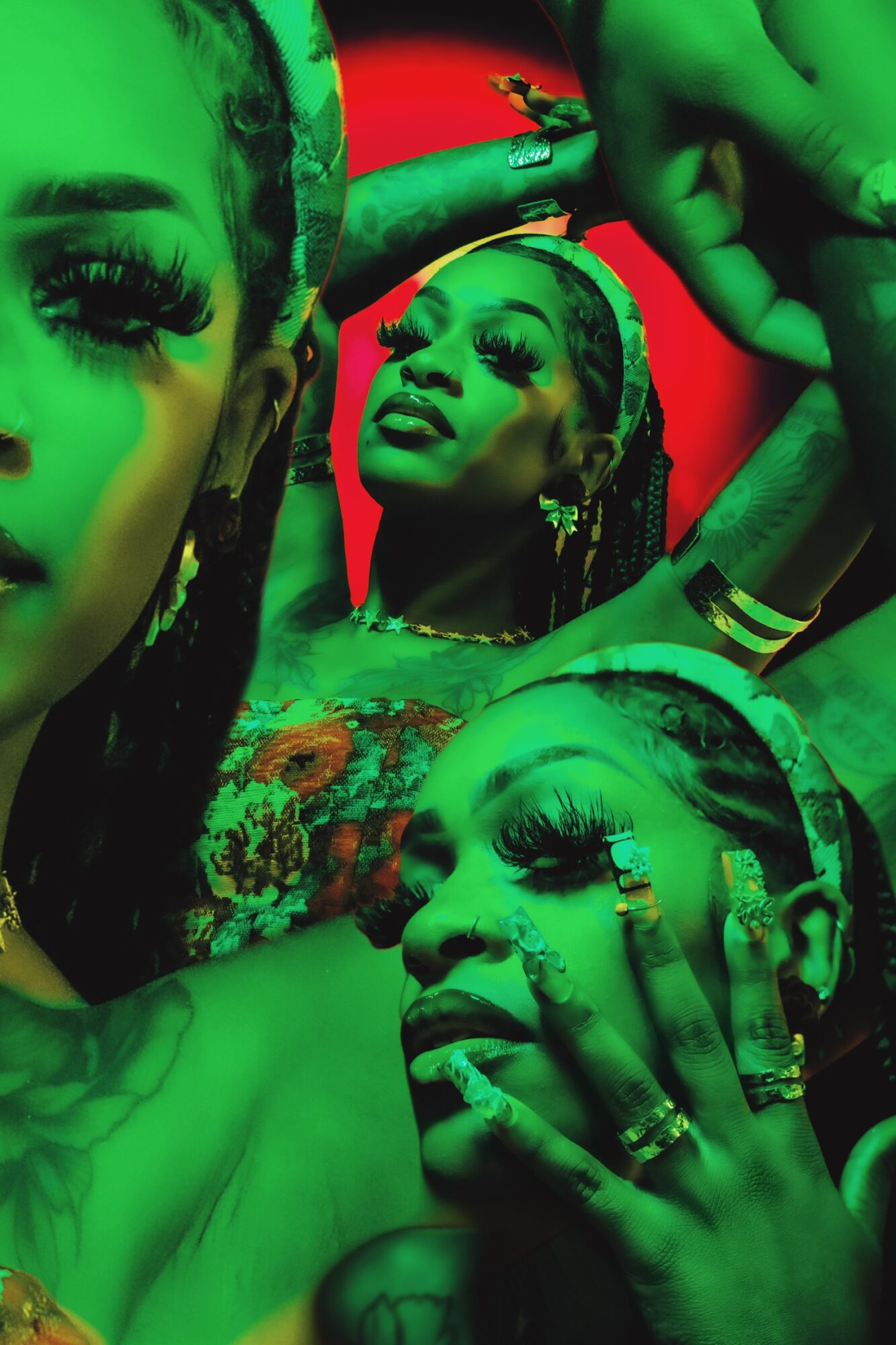 Three women with elaborate makeup and jewelry pose against a red and green background.