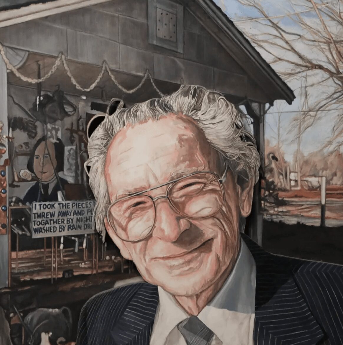 Portrait of an elderly man with glasses smiling outdoors, with a building and trees in the background.