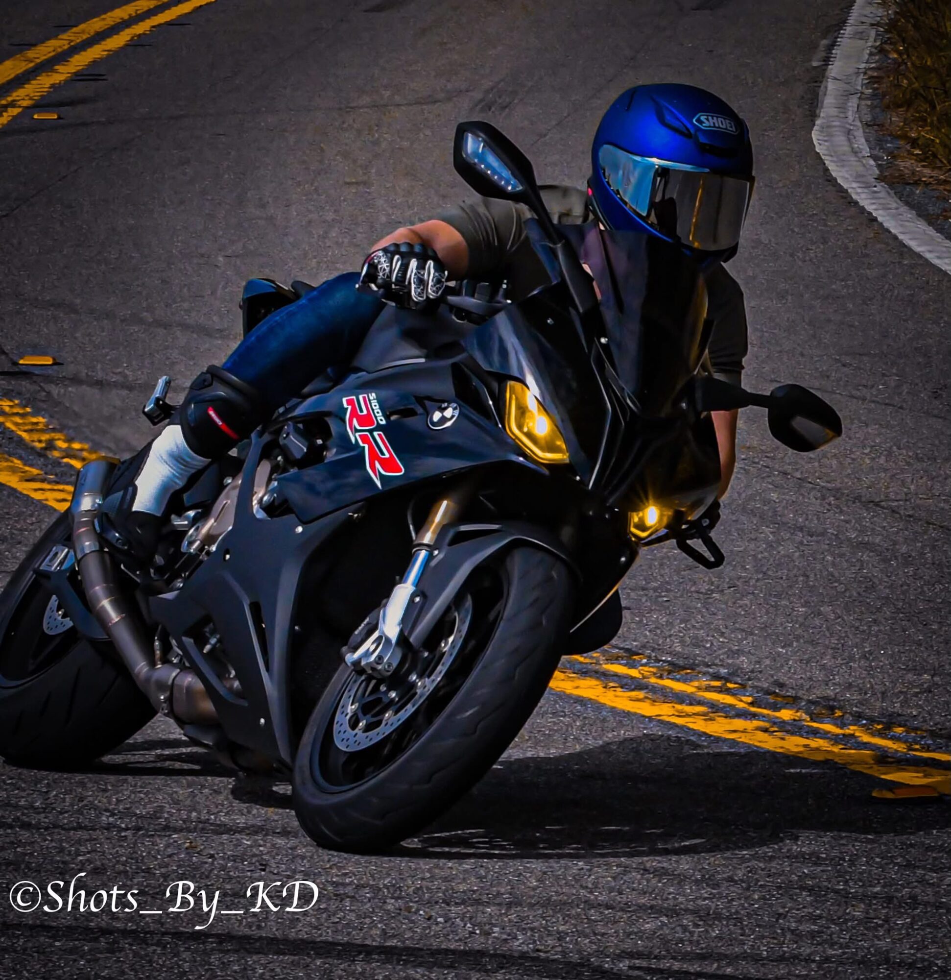 Motorcycle rider wearing a blue helmet leaning into a curve on a road, with yellow dividing lines.