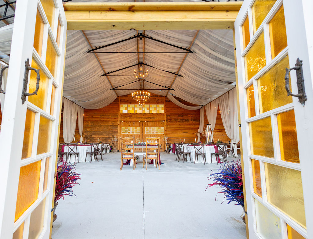 Open yellow doors reveal a decorated indoor event space with tables, chairs, and a chandelier, wooden walls, and draped ceiling.