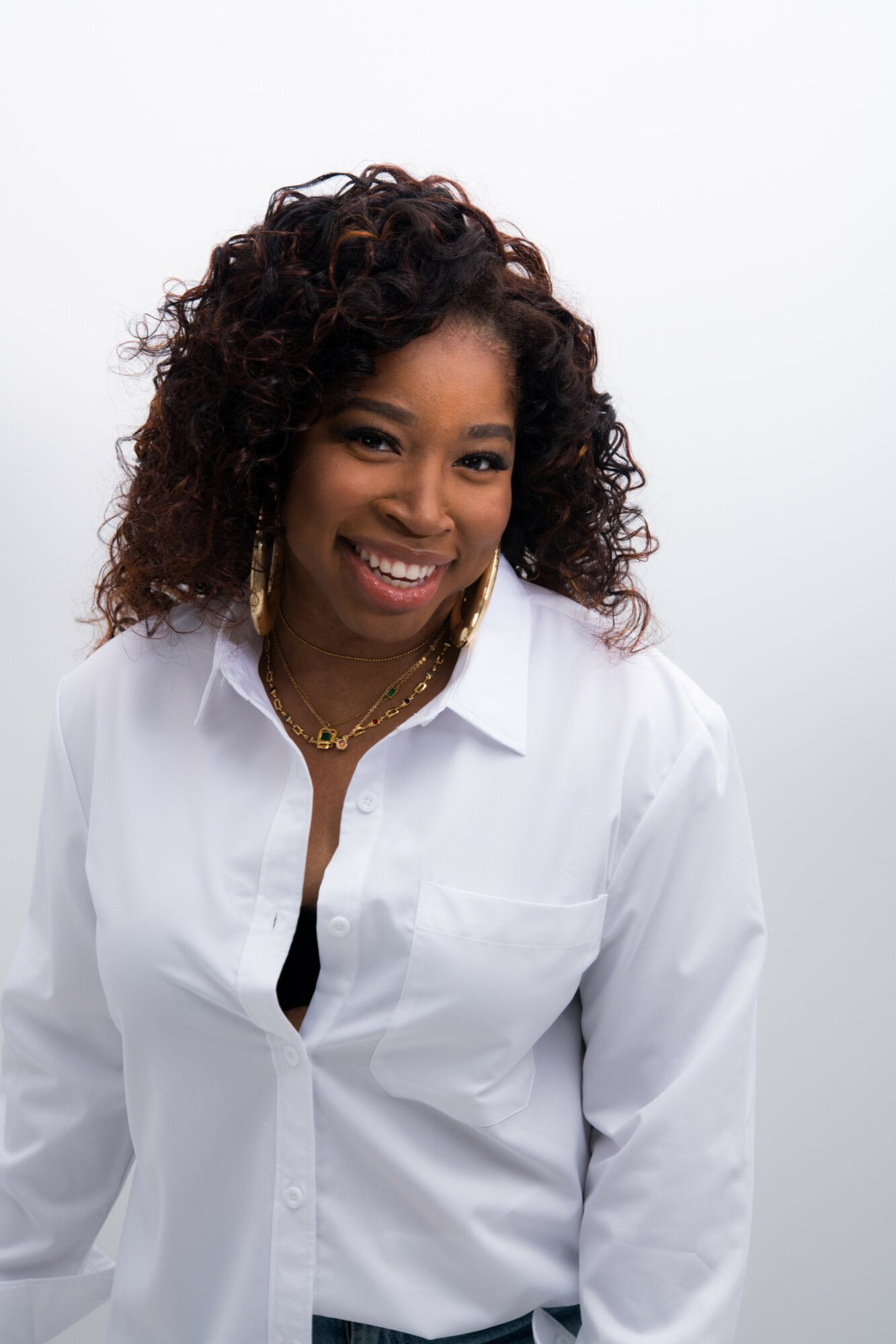 Smiling woman with curly hair wearing a white shirt against a plain background.